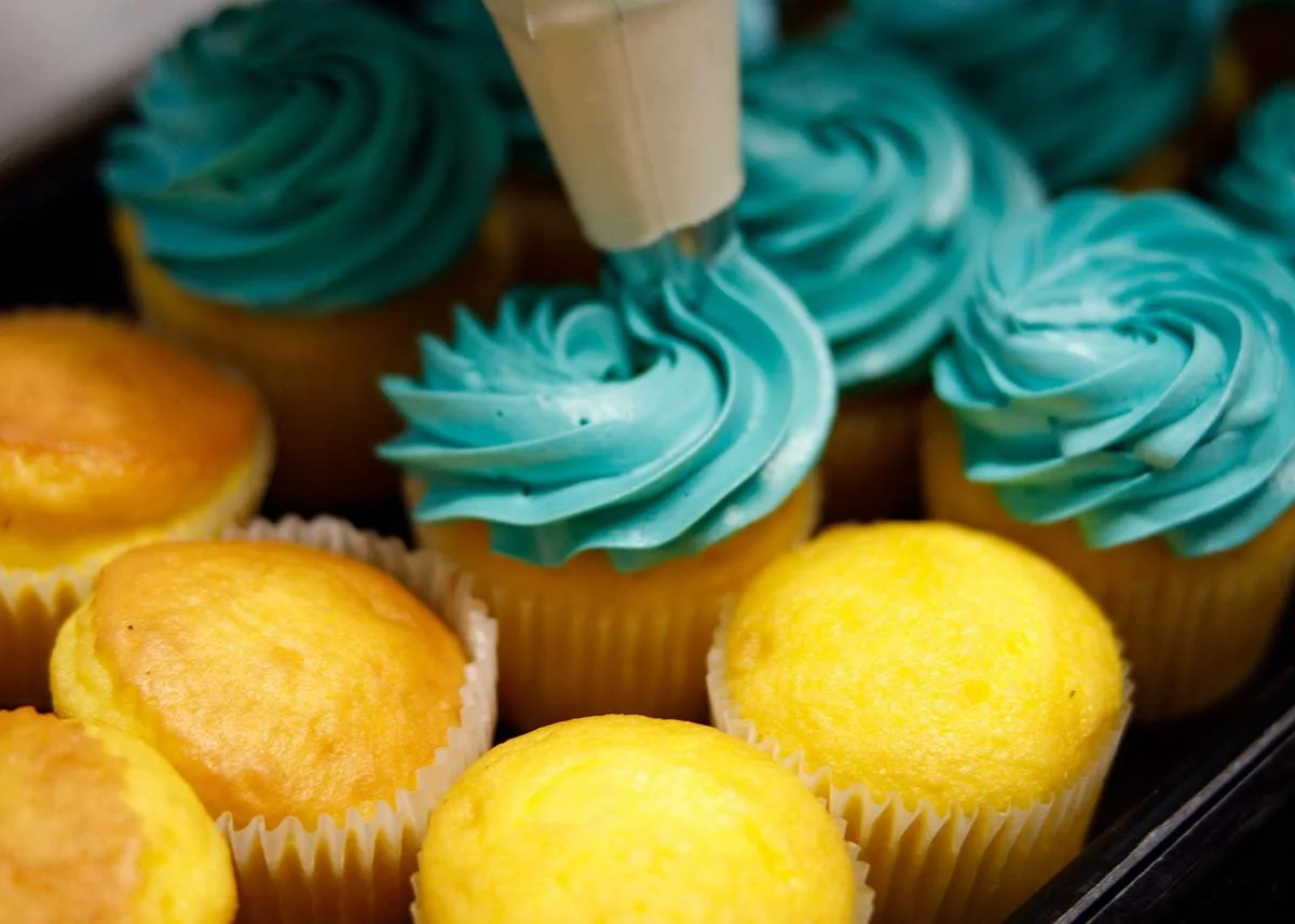 Blue-frosted cupcakes decorated with piped swirls alongside plain yellow cupcakes