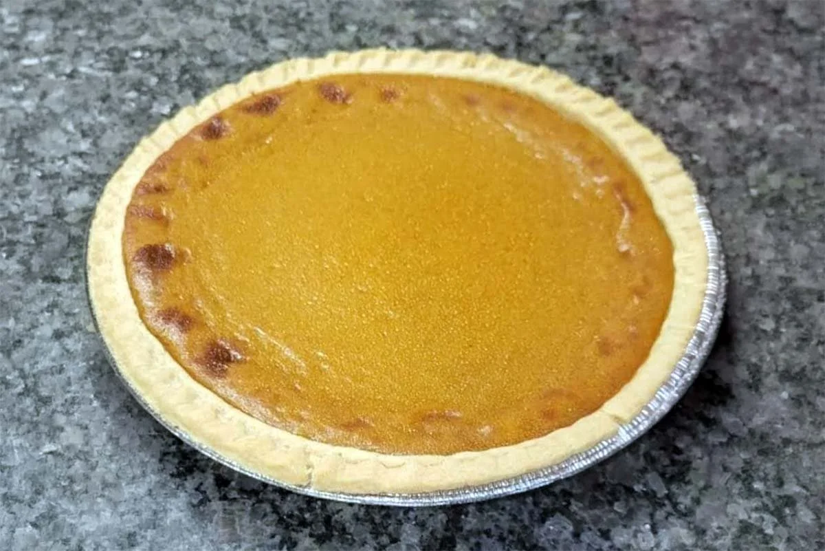 Golden-brown pumpkin pie in a crimped pastry crust on a foil pie pan.