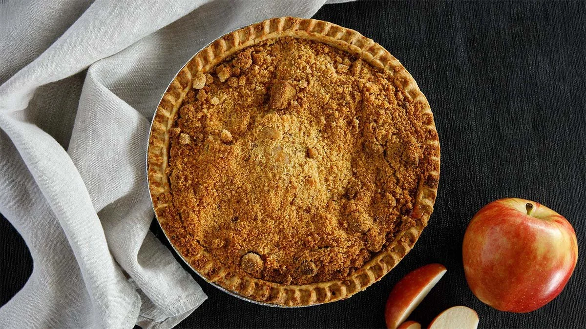 Homemade apple pie with crumb topping, whole apple, and apple slices