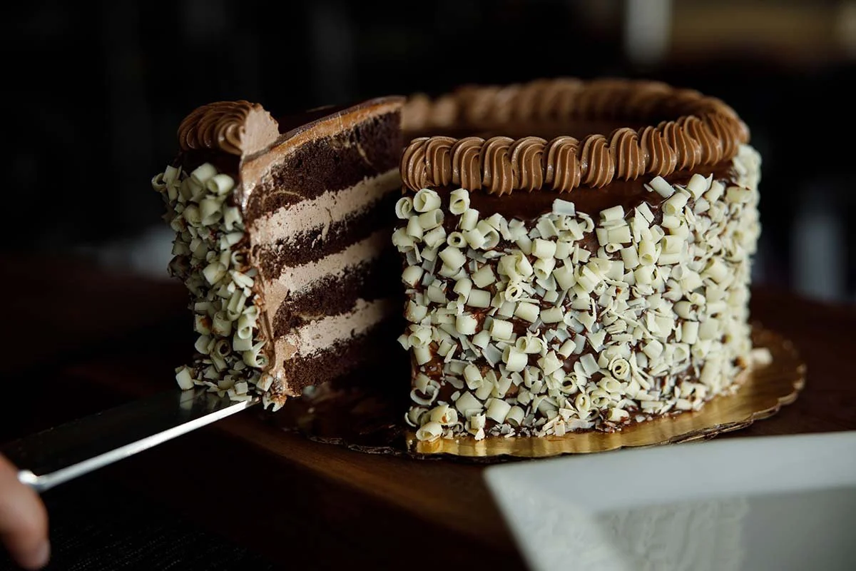 Chocolate layer cake covered in white chocolate curls, with a slice being served.