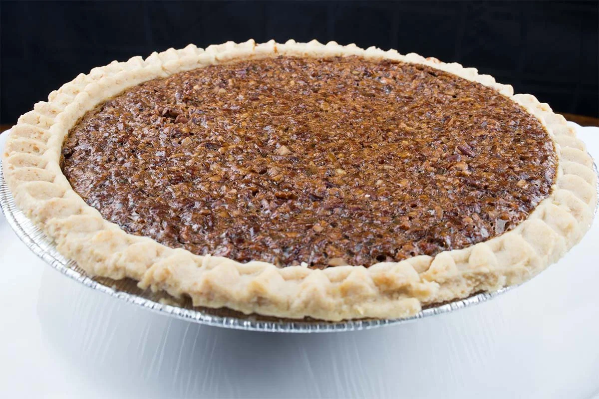 Whole pecan pie with a flaky crimped crust in a foil pie pan
