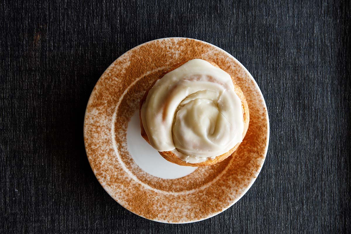 Top-down view of a cinnamon roll with creamy white frosting on a decorative plate.