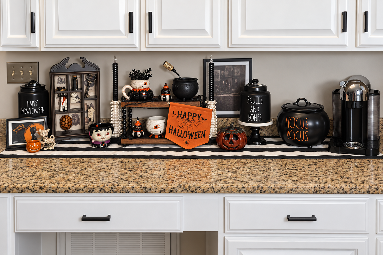 Halloween-themed decorations on a kitchen countertop, including pumpkin figures, black jars labeled "Skulls and Bones" and "Hocus Pocus," small figurines, and a "Happy Halloween" banner, with white cabinets above and a coffee machine on the right.