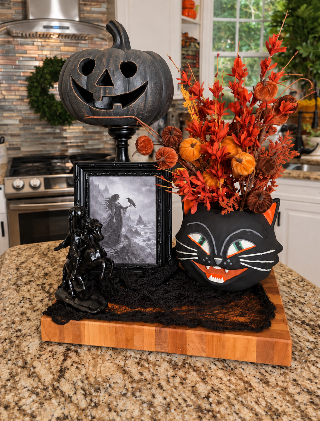 Halloween décor vignette with jack-o'-lanterns, black cat figure, framed art, and orange floral arrangement.