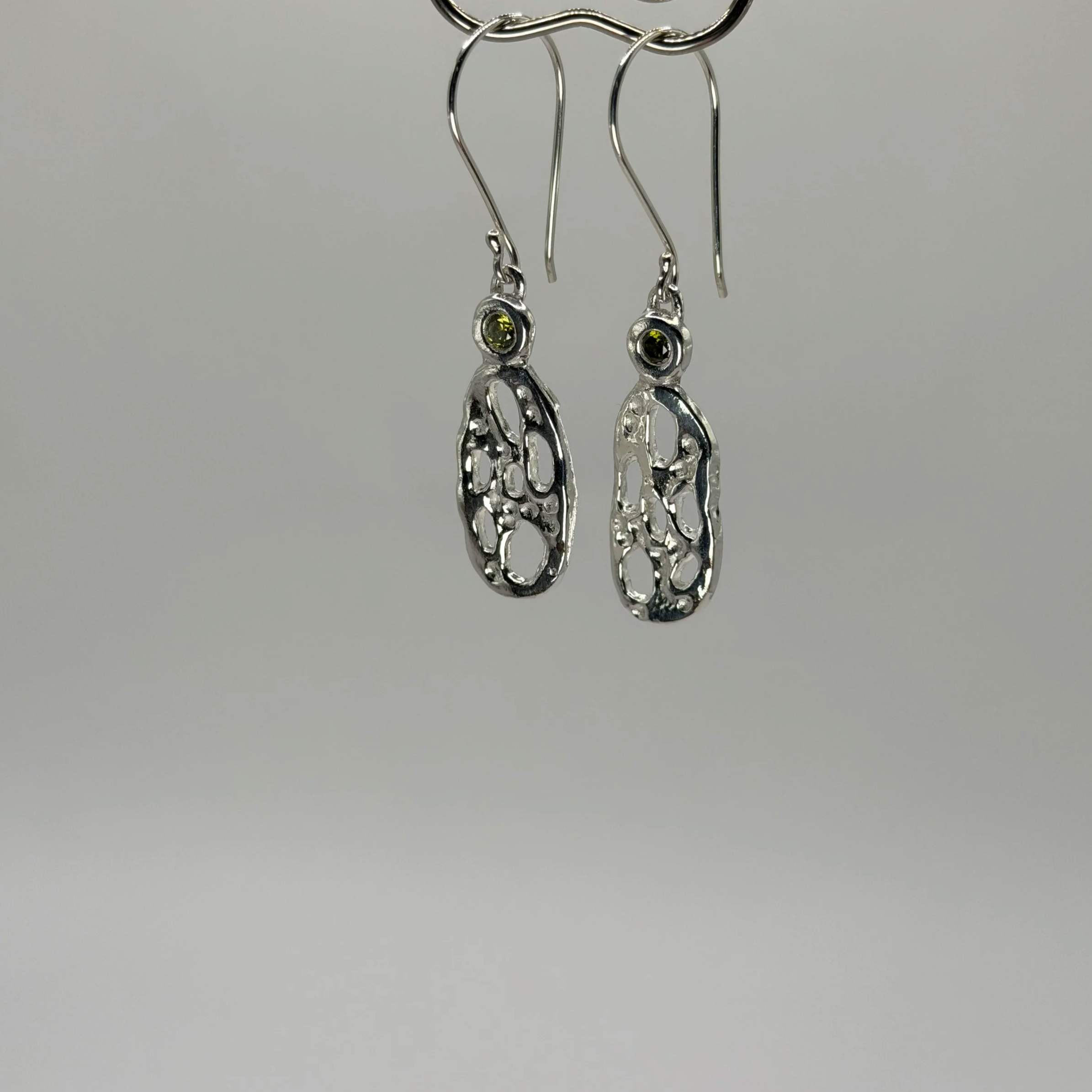 Sculptural fine silver drop earrings with organic detailing and green cubic zirconia stones, handmade by Avila Jewellery Designs.