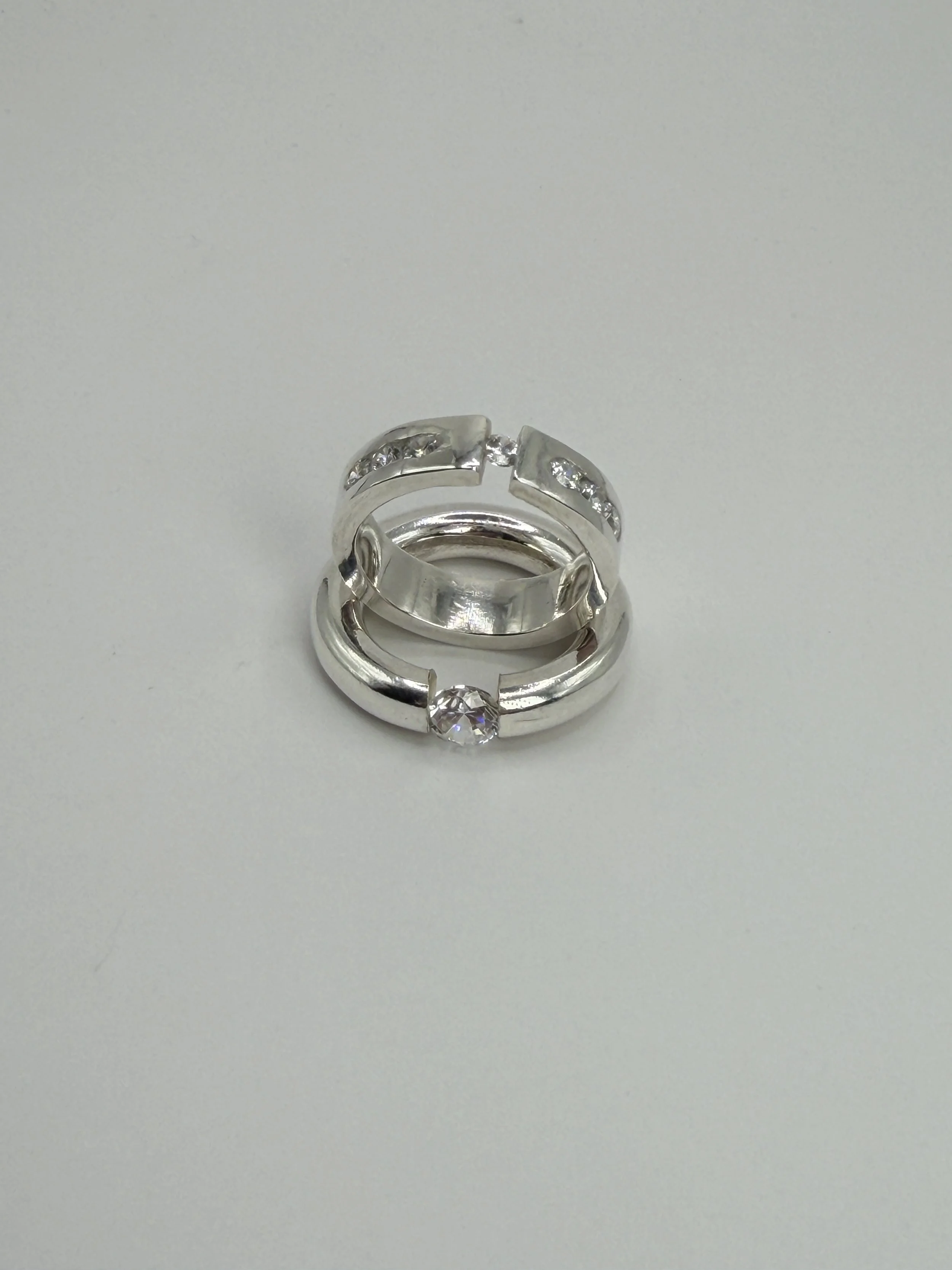 Two sterling silver rings with clear cubic zirconia stones, one tension-set and one featuring a tension-set centre stone with channel-set stones along the shoulders, handmade by Avila Jewellery Designs.