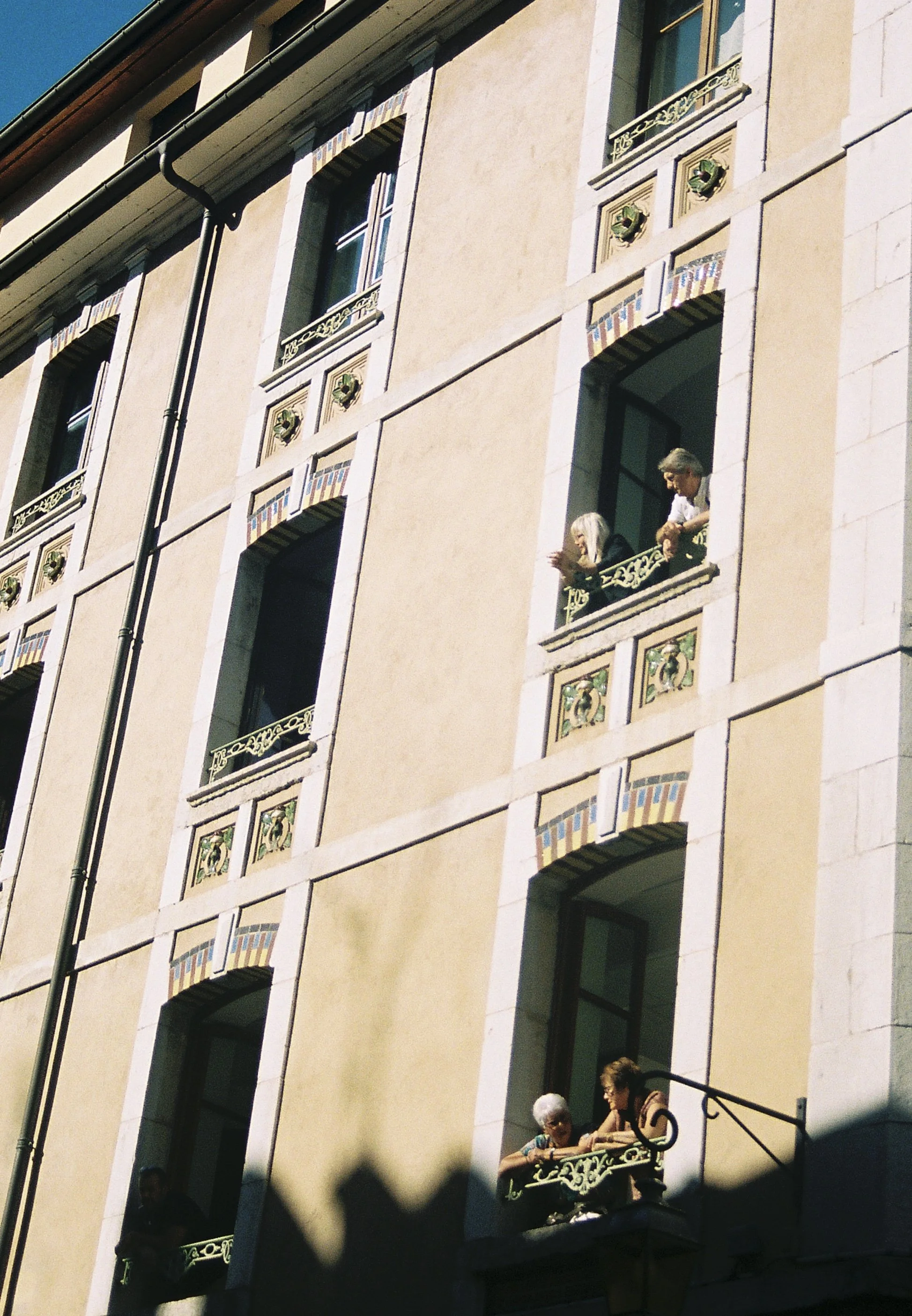 Three elderly women and a middle-aged woman with glasses on a building's balcony in Europe.