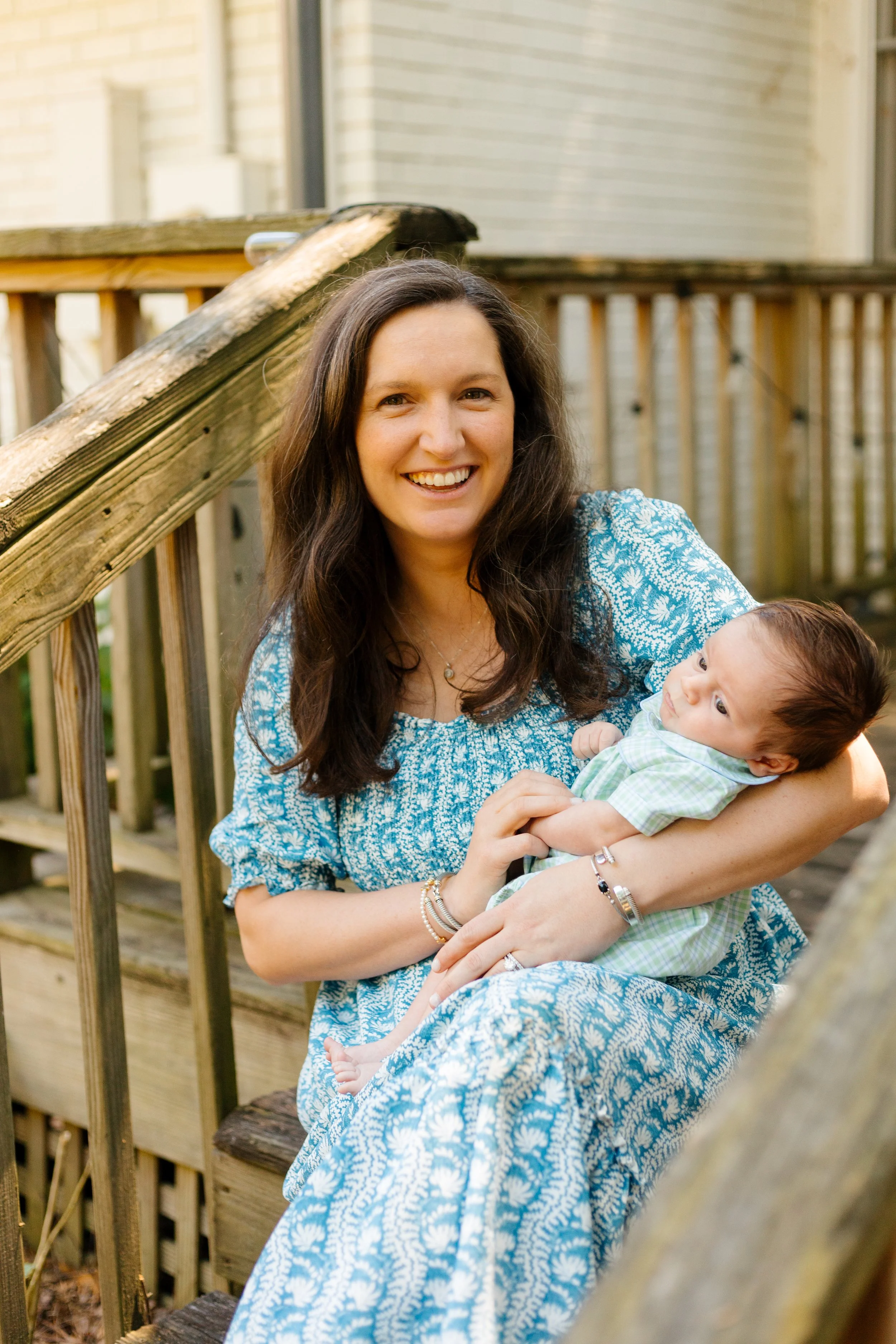 Woman in a teal floral dress holding her newborn on a wooden deck