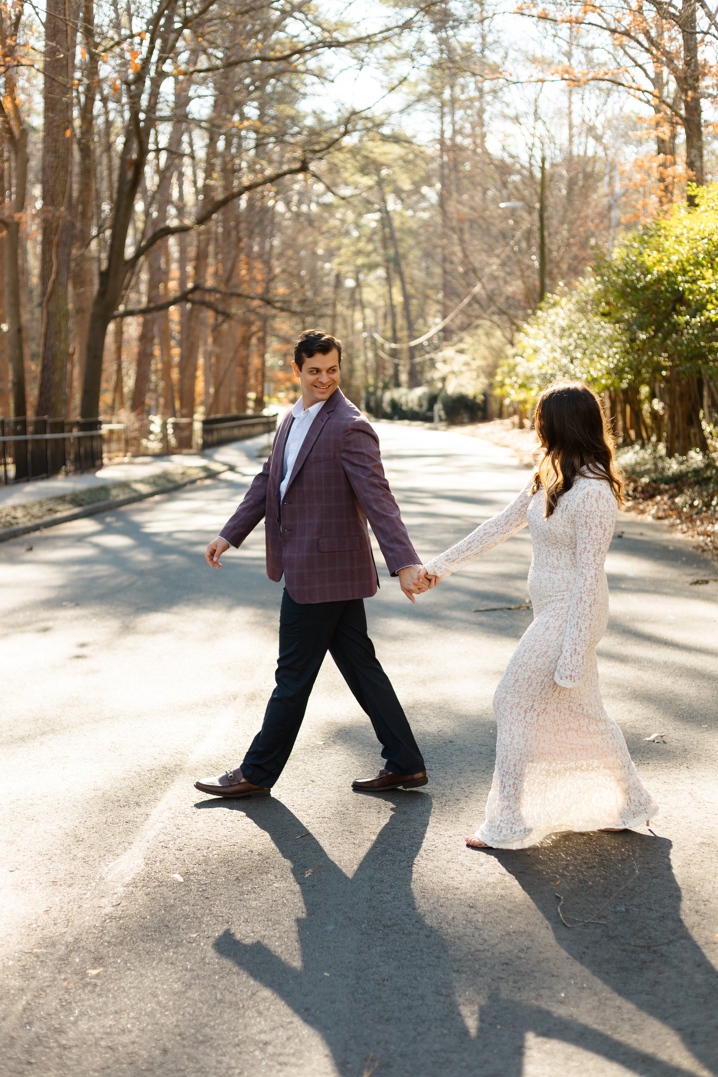 Engaged couple walking hand-in-hand down a tree-lined street.
