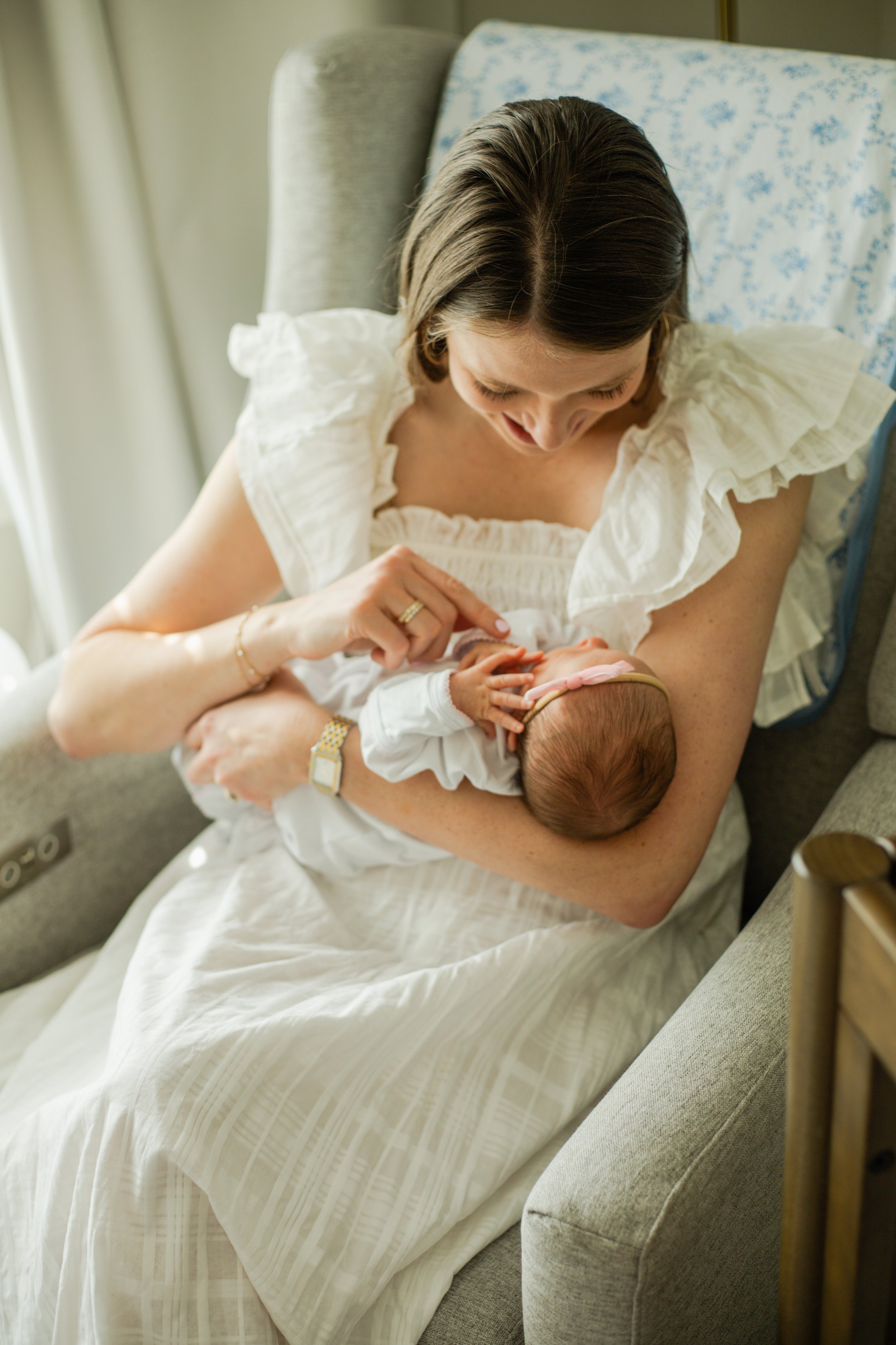 Mother with her newborn in a lace dress, candid moment in nursery. 