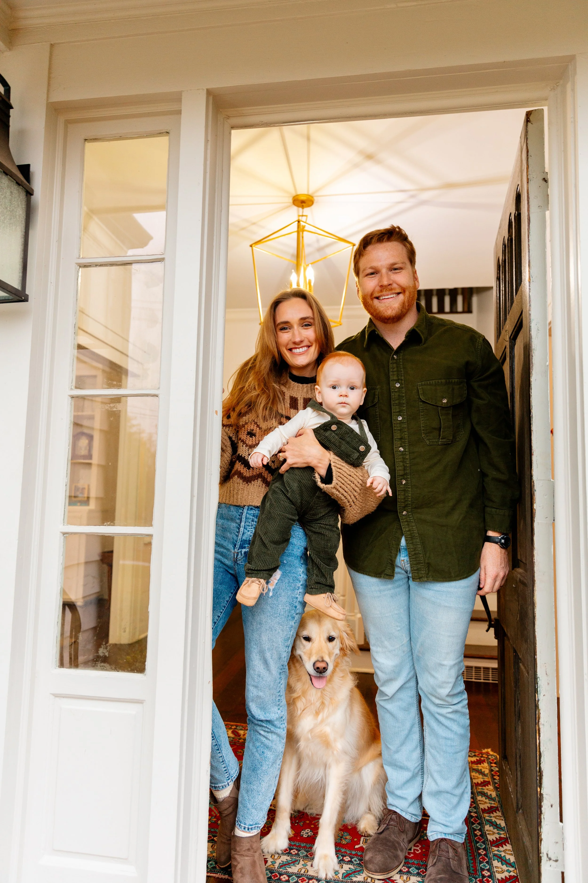 A happy family of three with a golden retriever dog standing at the front door of their home. 