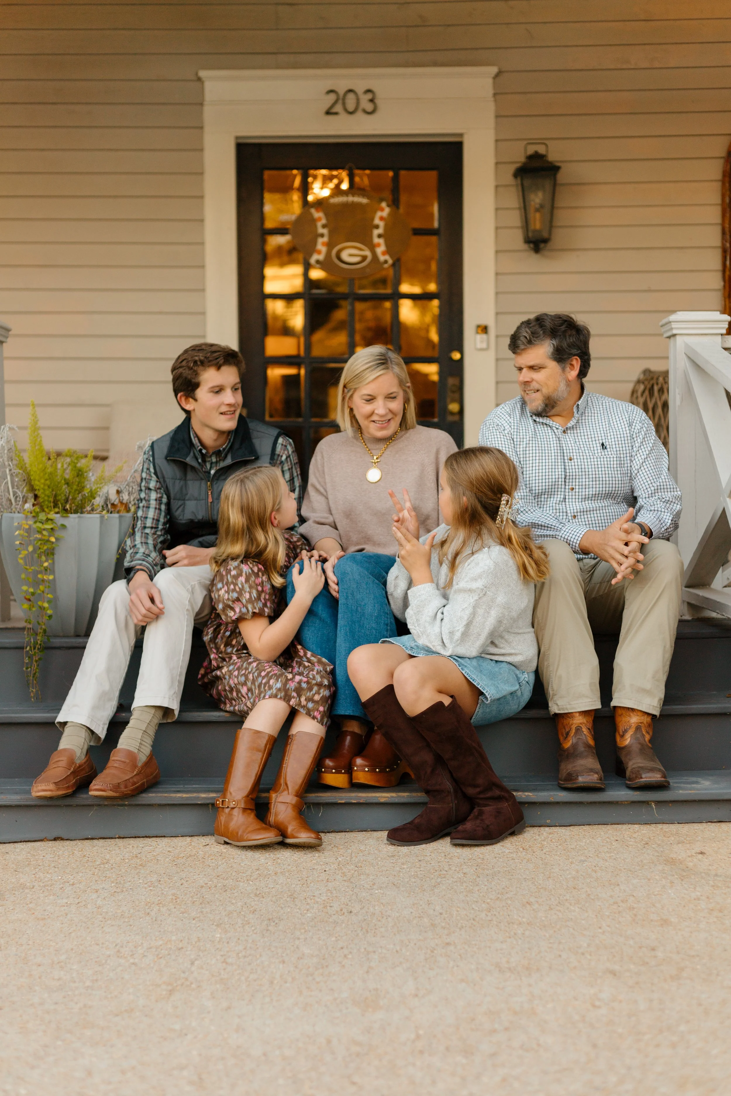 Family of five sitting together on front porch steps during a Christmas card photo session. 