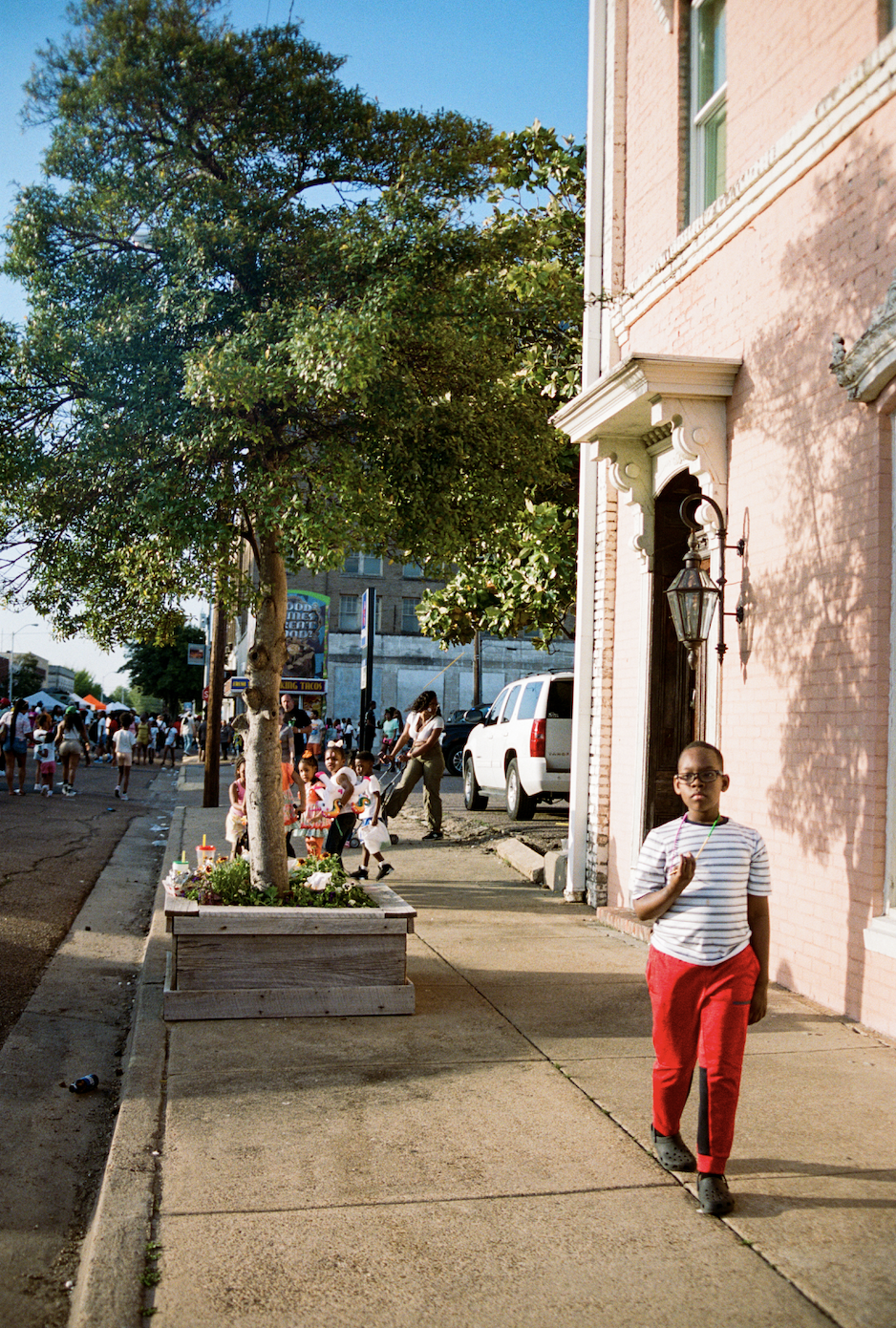 Child walking along a sidewalk past a pink building in Clarksdale, Mississippi for the Juke Joint Blues Festival