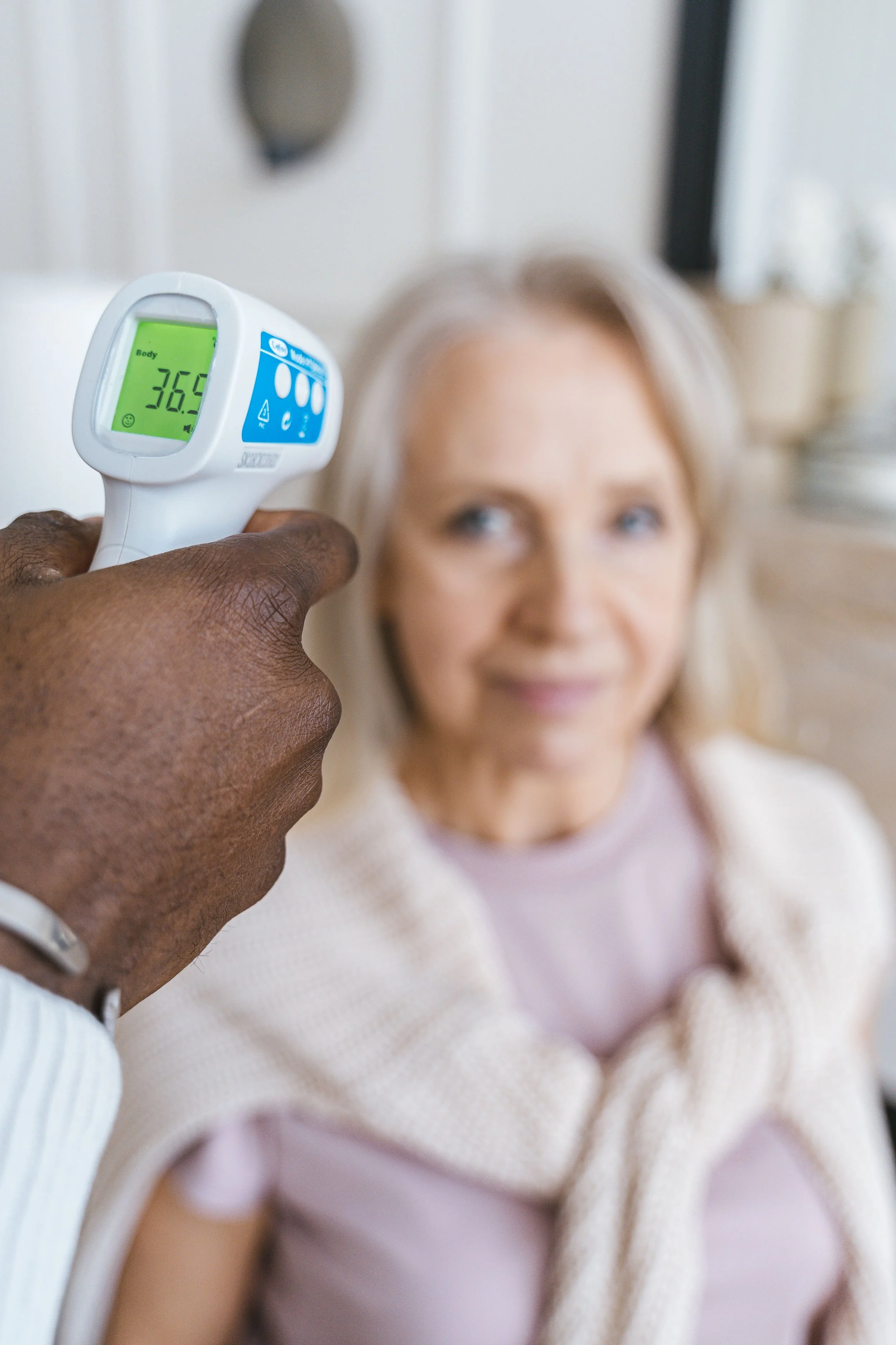 An on-site medical professional assessing vitals using a digital thermometer to conduct a clinical assessment on a senior resident.