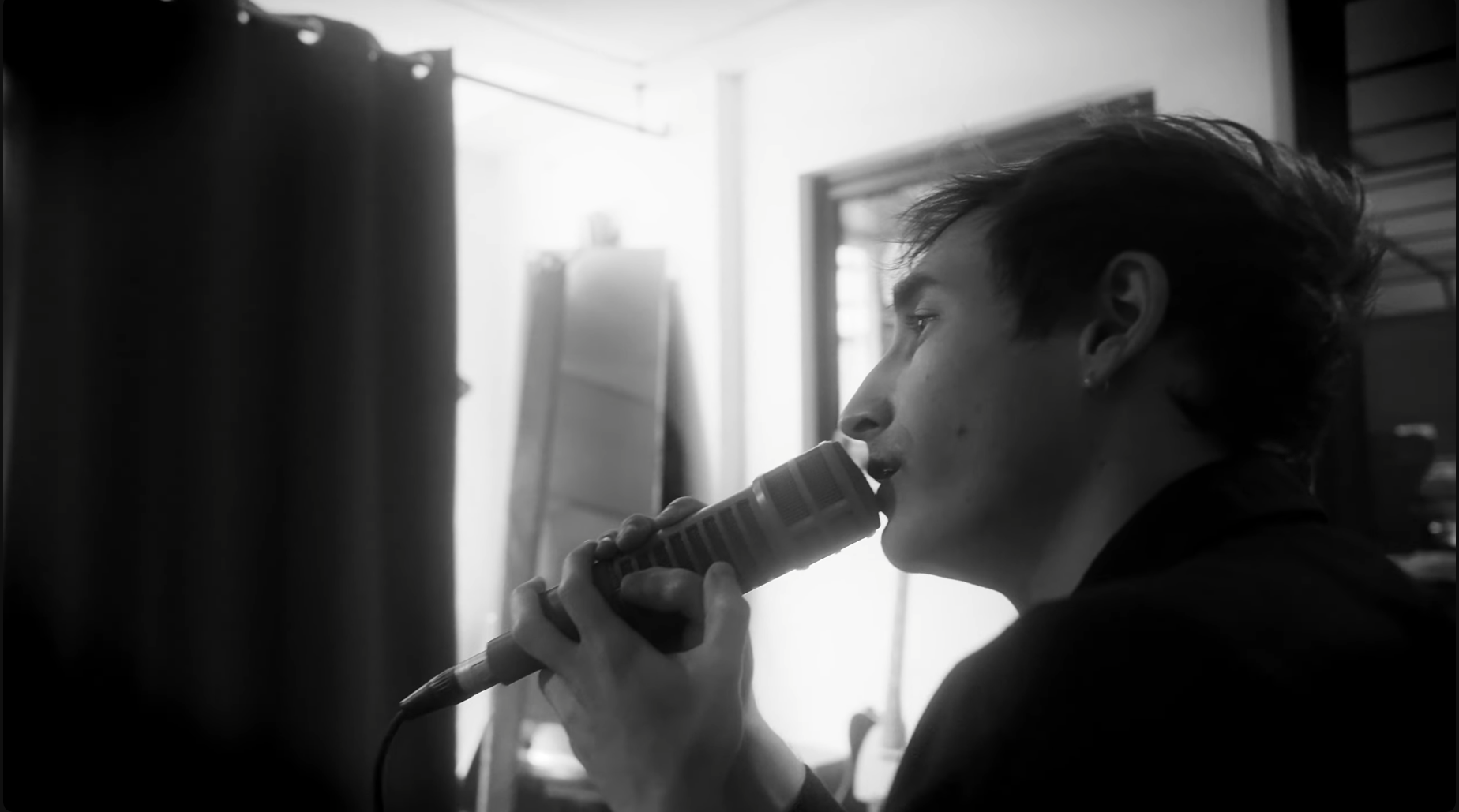 Un jeune homme souriant joue et chante, en noir et blanc.