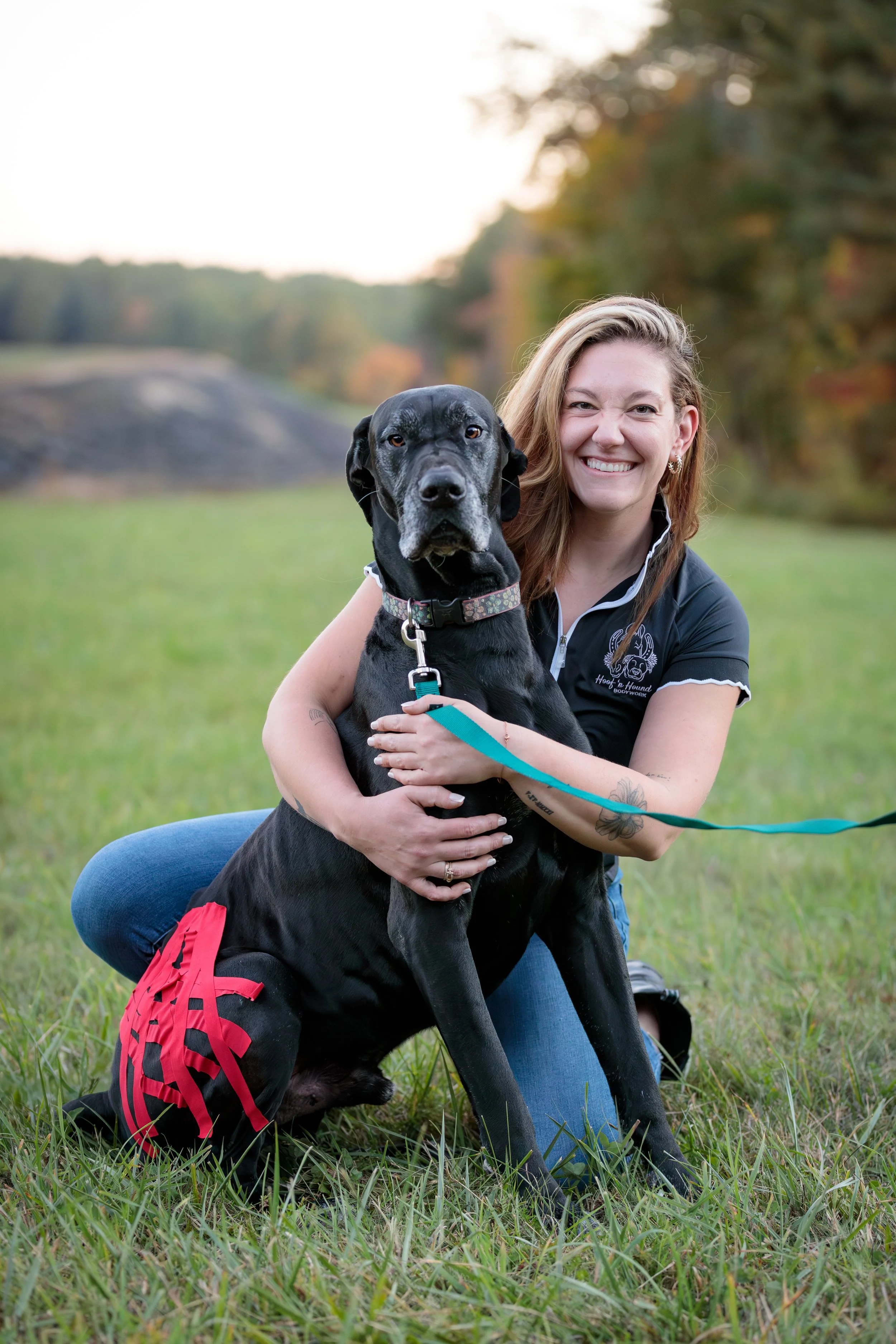 Smiling woman sitting in a grassy field with a large black dog during a training session