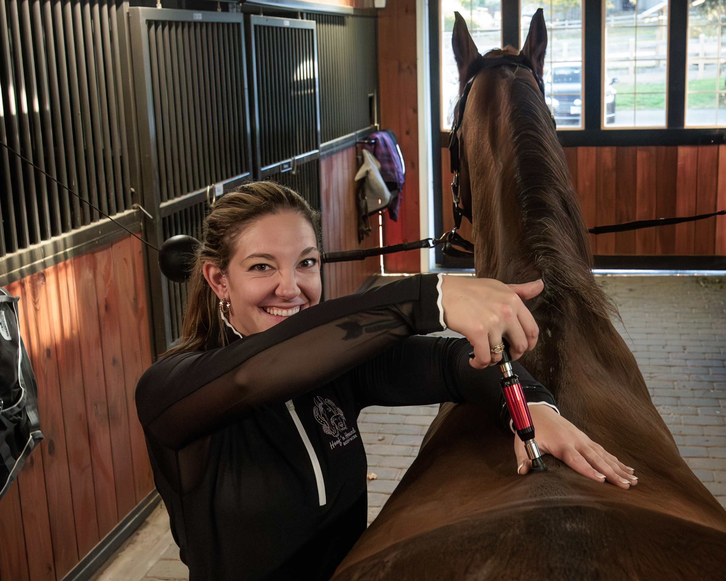 Woman using a syringe-like applicator on a horse’s back inside a stable