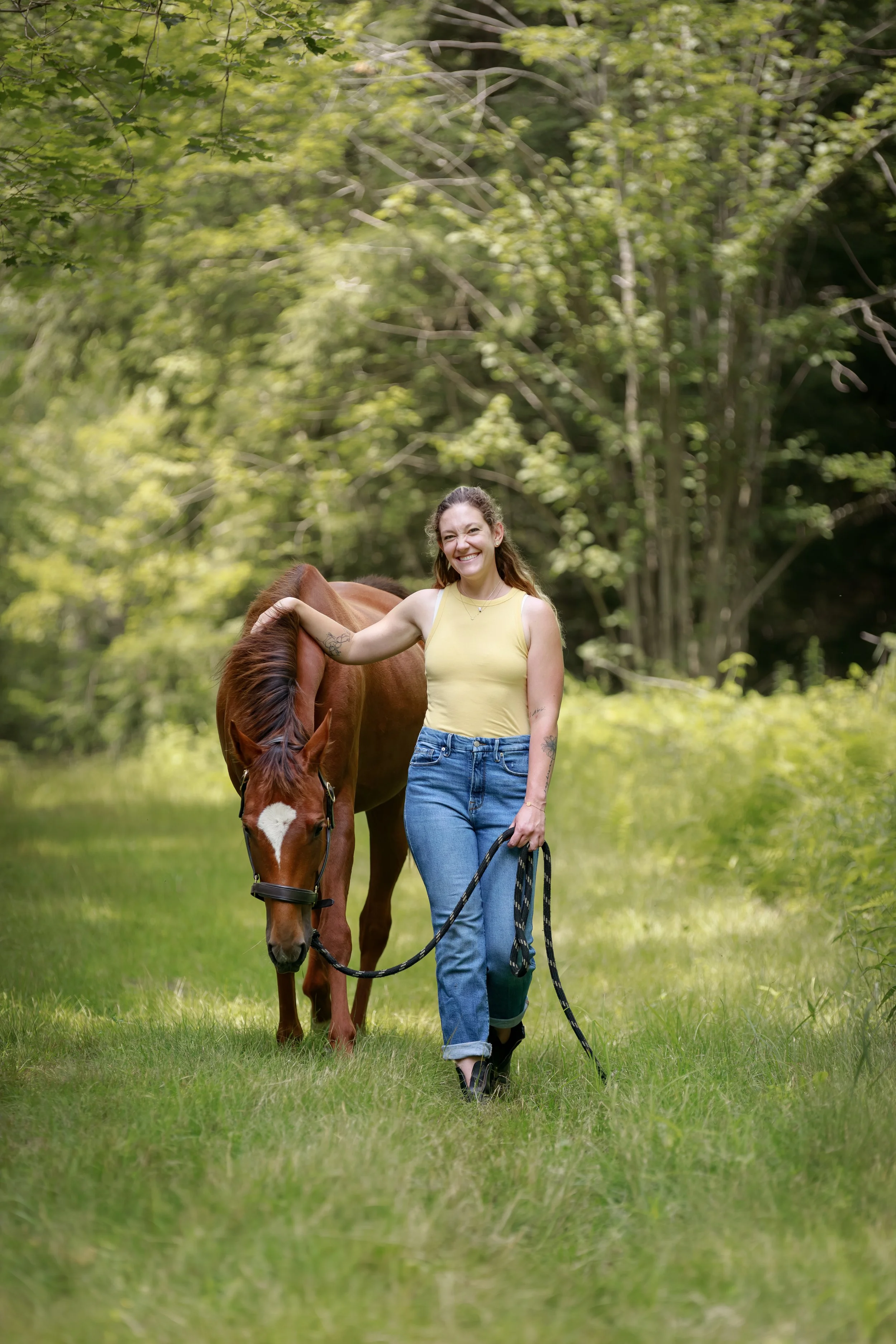Smiling woman walking through a grassy field beside a brown horse on a lead rope