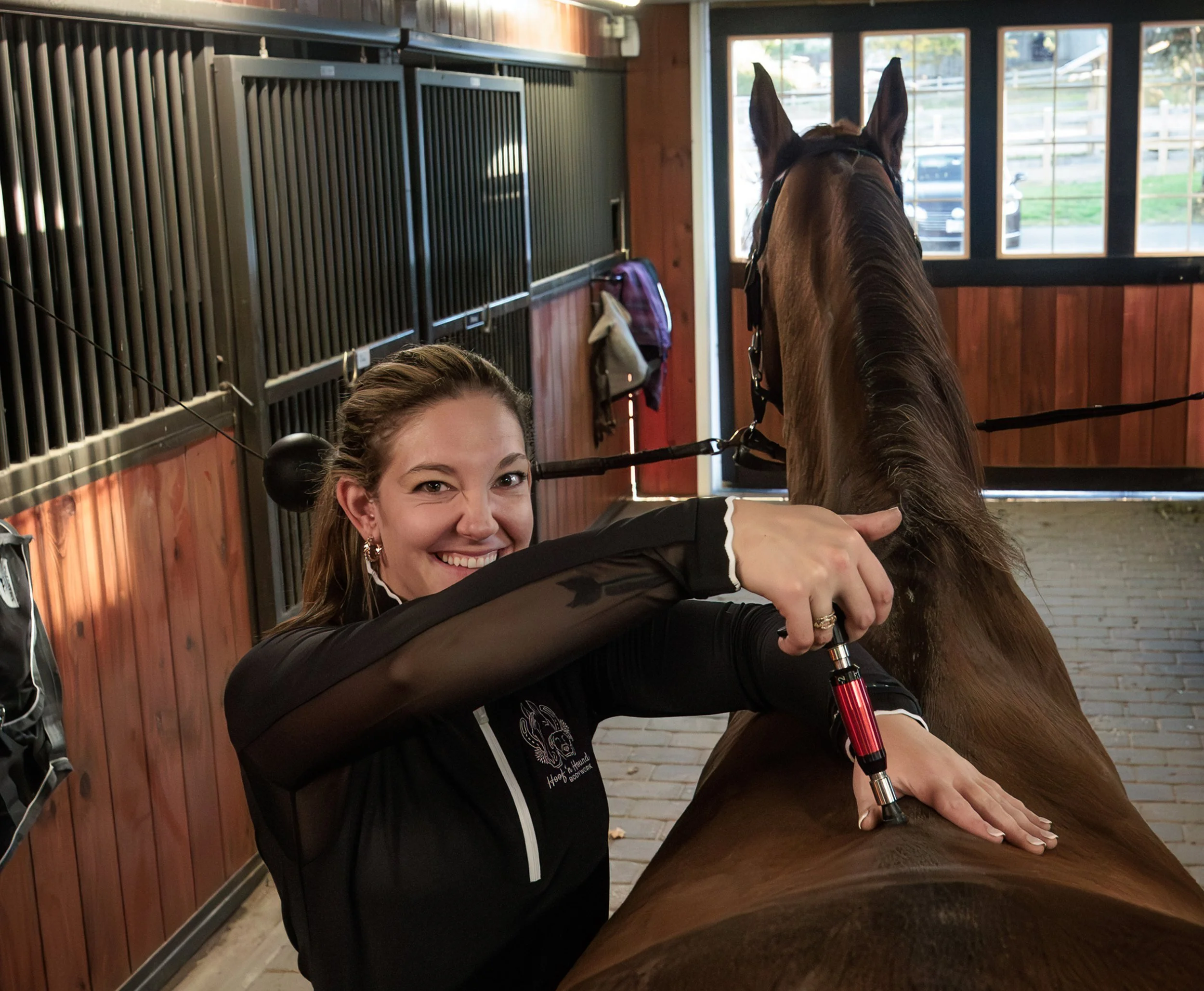 Woman using a syringe-like applicator on a horse’s back inside a stable