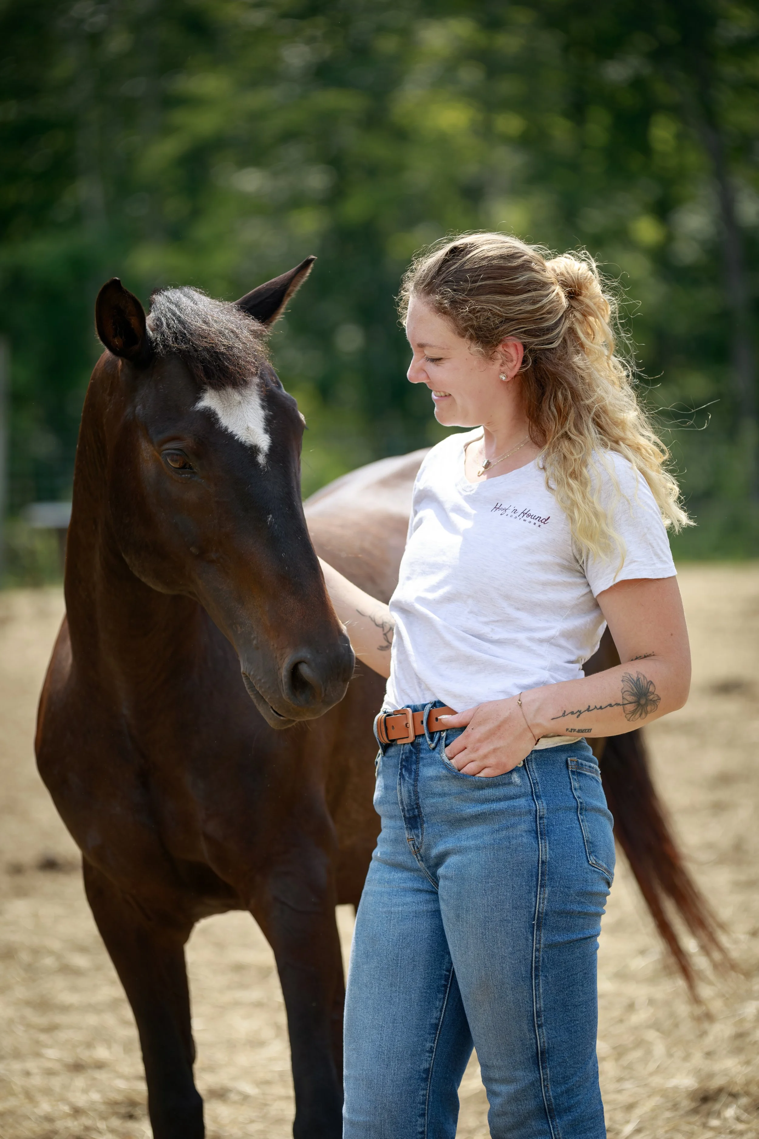 Woman smiling beside a dark brown horse outdoors in a sunny field