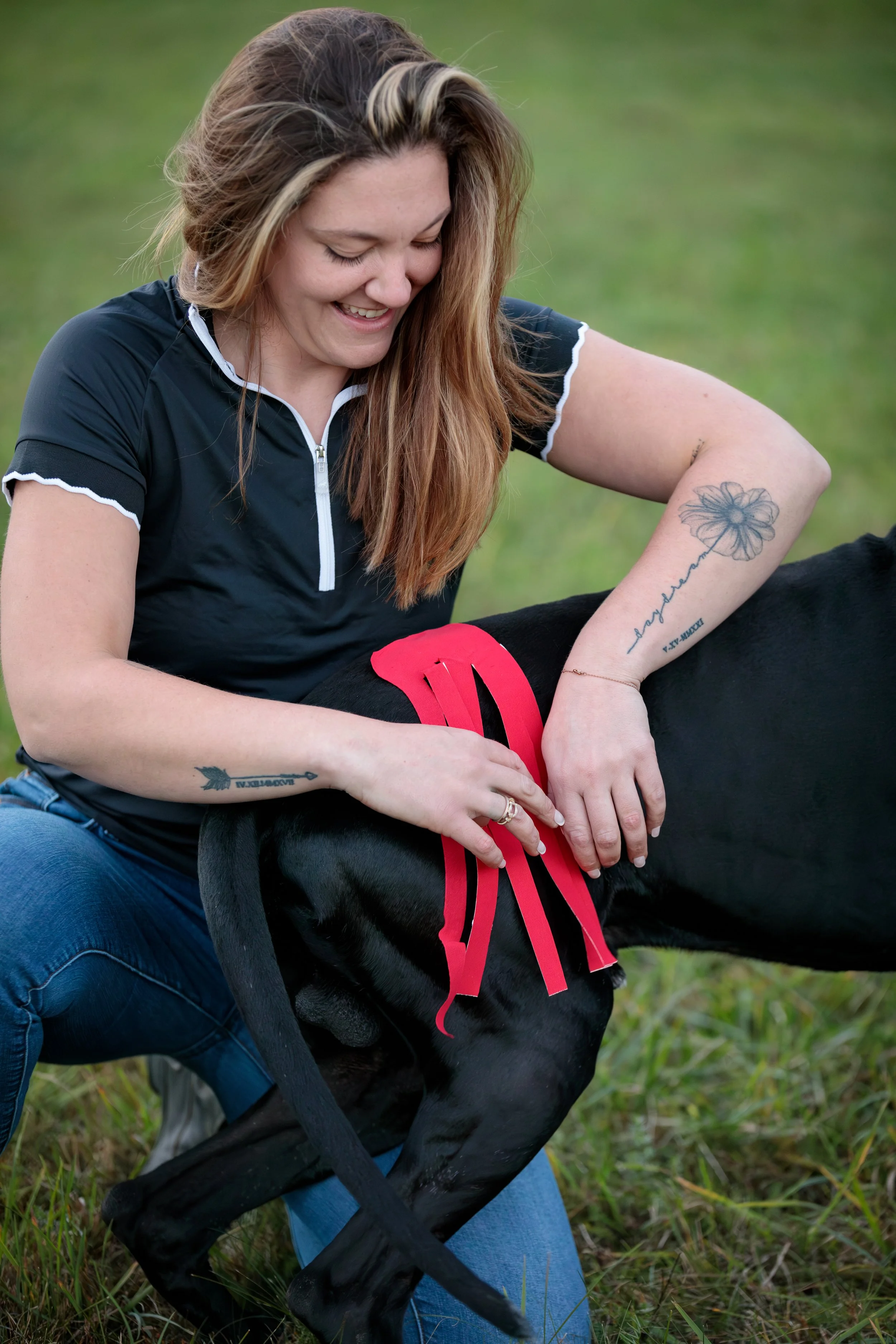 Woman applying bright red kinesiology tape to a black dog’s hind leg
