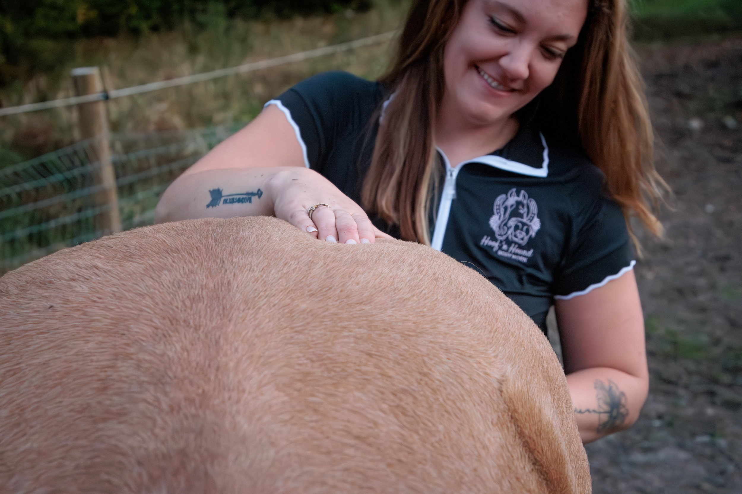 Woman smiling while performing myofascial release therapy on a brown horse outdoors