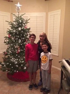 A mother and her two sons decorating a Christmas tree together at home