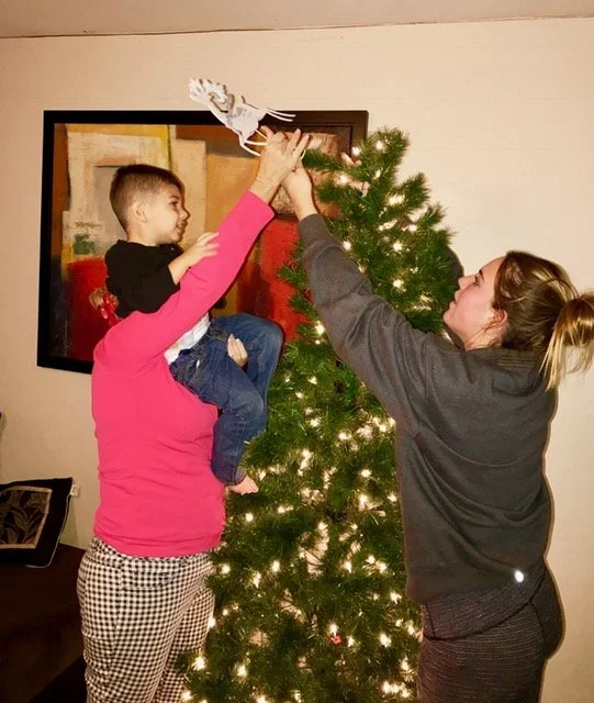 A mother lifting her son up to hang an ornament on the family Christmas tree