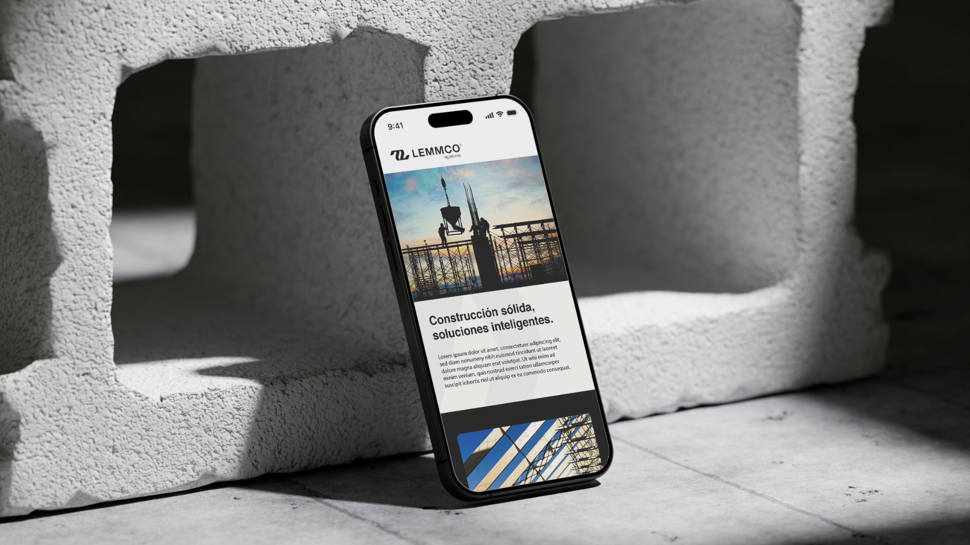 Teléfono móvil en una estructura de block con la pantalla mostrando una página web de una empresa de construcción llamada LEMMCO, con una imagen de un andamio y la frase 'Construcción sólida, soluciones inteligentes'.