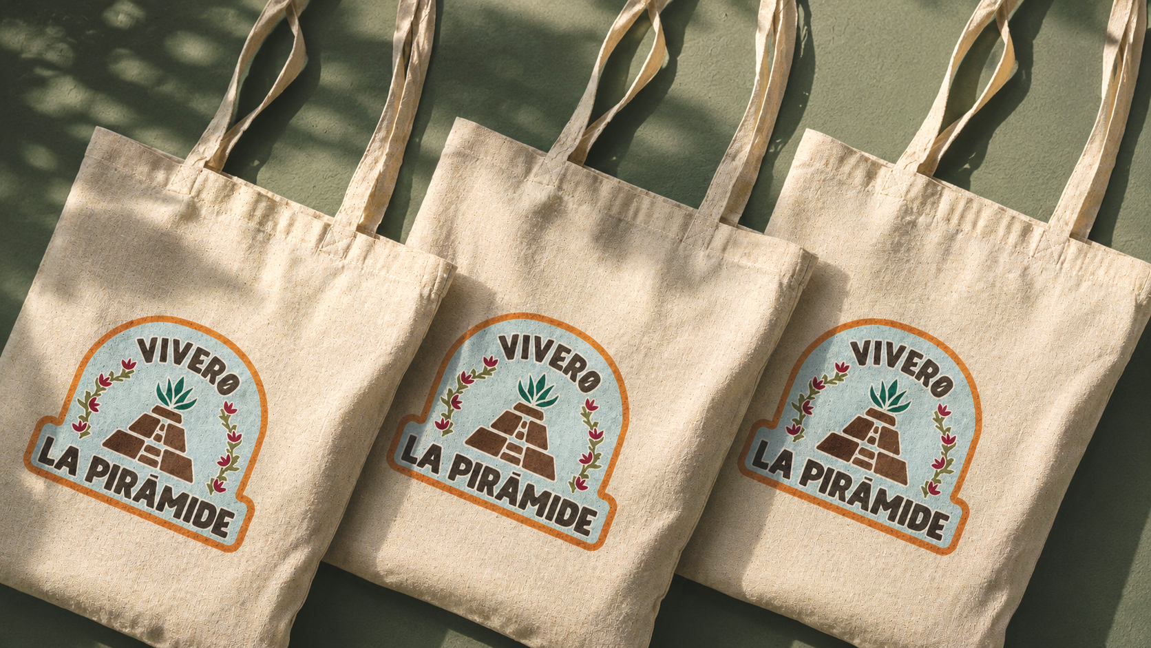 Tres bolsas de tela con un logotipo que dice 'Vivere La Pirámide' y muestra una pirámide con plantas creciendo en ella, rodeada de hojas y ramas decorativas.