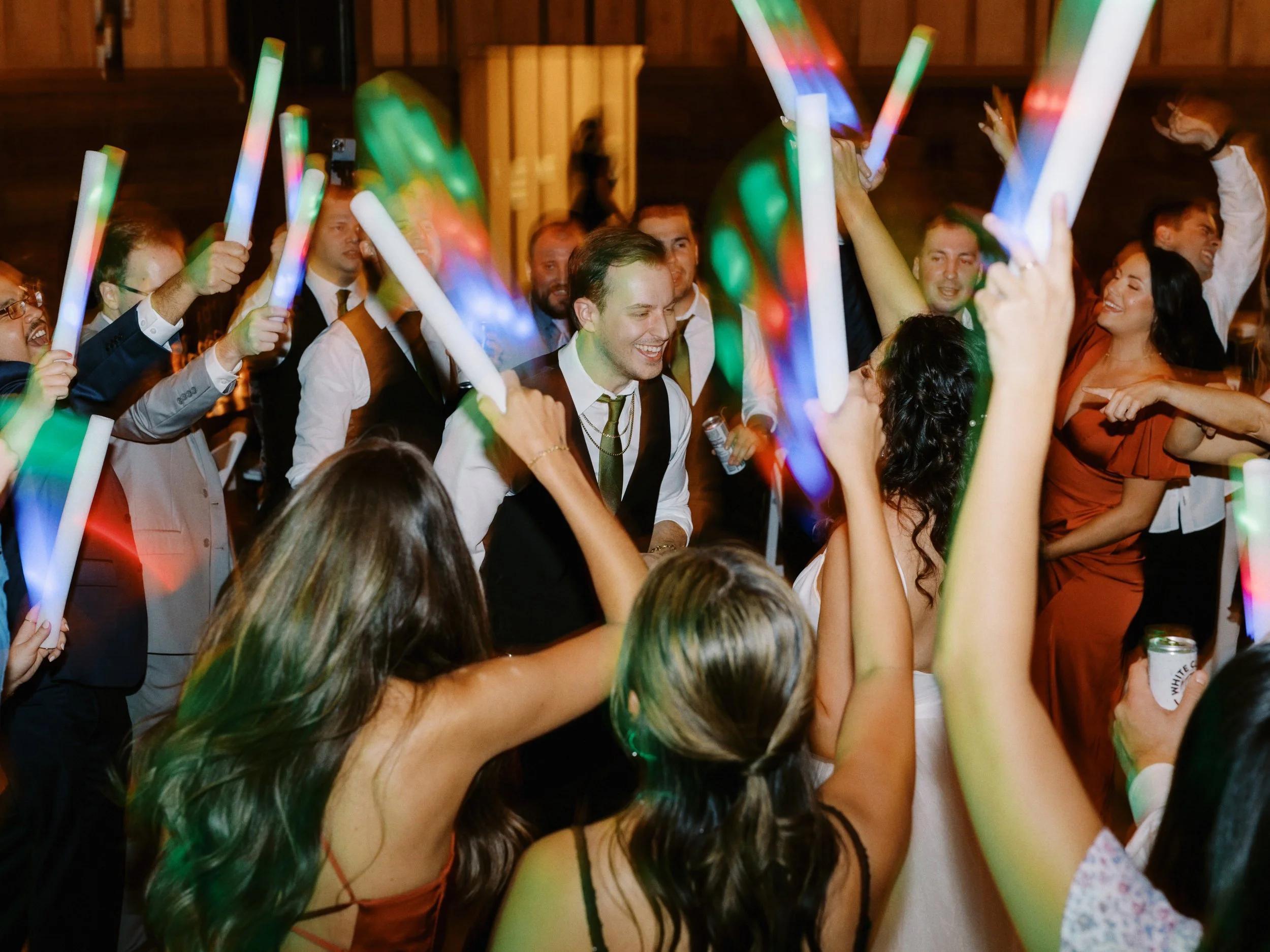 A lively indoor party scene with people dancing and holding glow sticks at night.