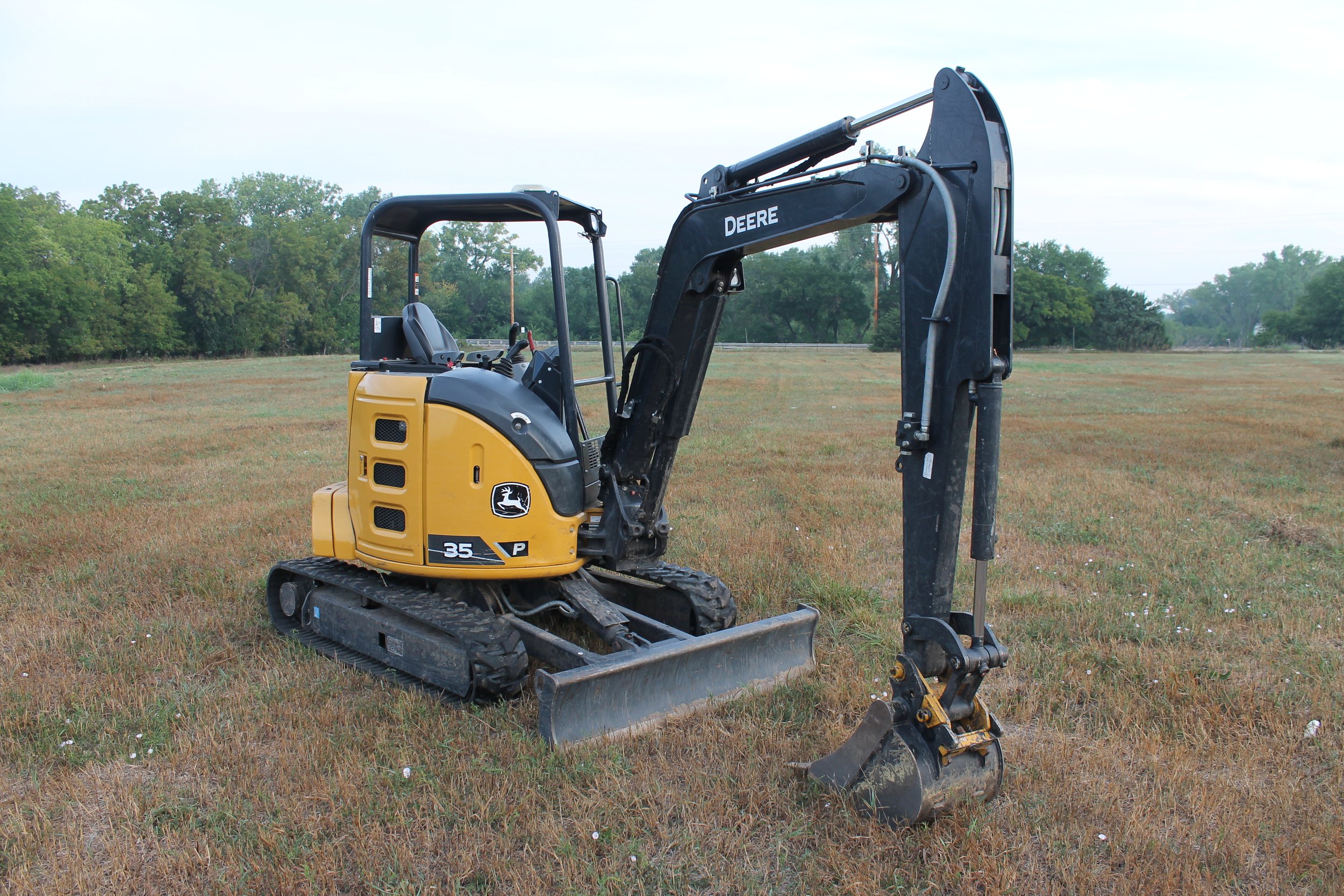 A small John Deere excavator sitting on a grassy field with trees in the background.