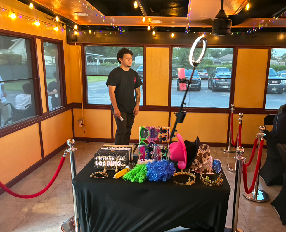 A person standing inside a decorated party room with colorful string lights, a table with various costume accessories like hats and headbands, and a sign that reads 'Future CEO Loading...'.