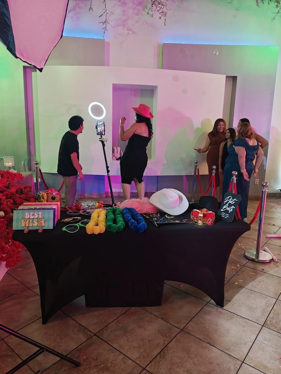 People at a photo booth with colorful decorations, props like hats and boas, and a sign that says 'Best Wish'.