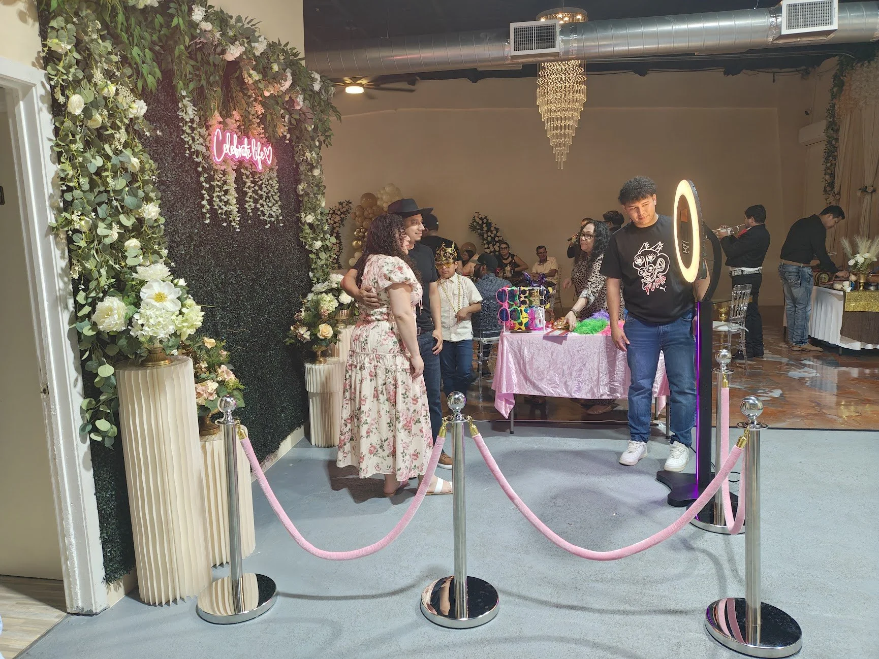 People attending a celebration event with floral decorations, balloons, and a sign that says 'Celebrate Love'.