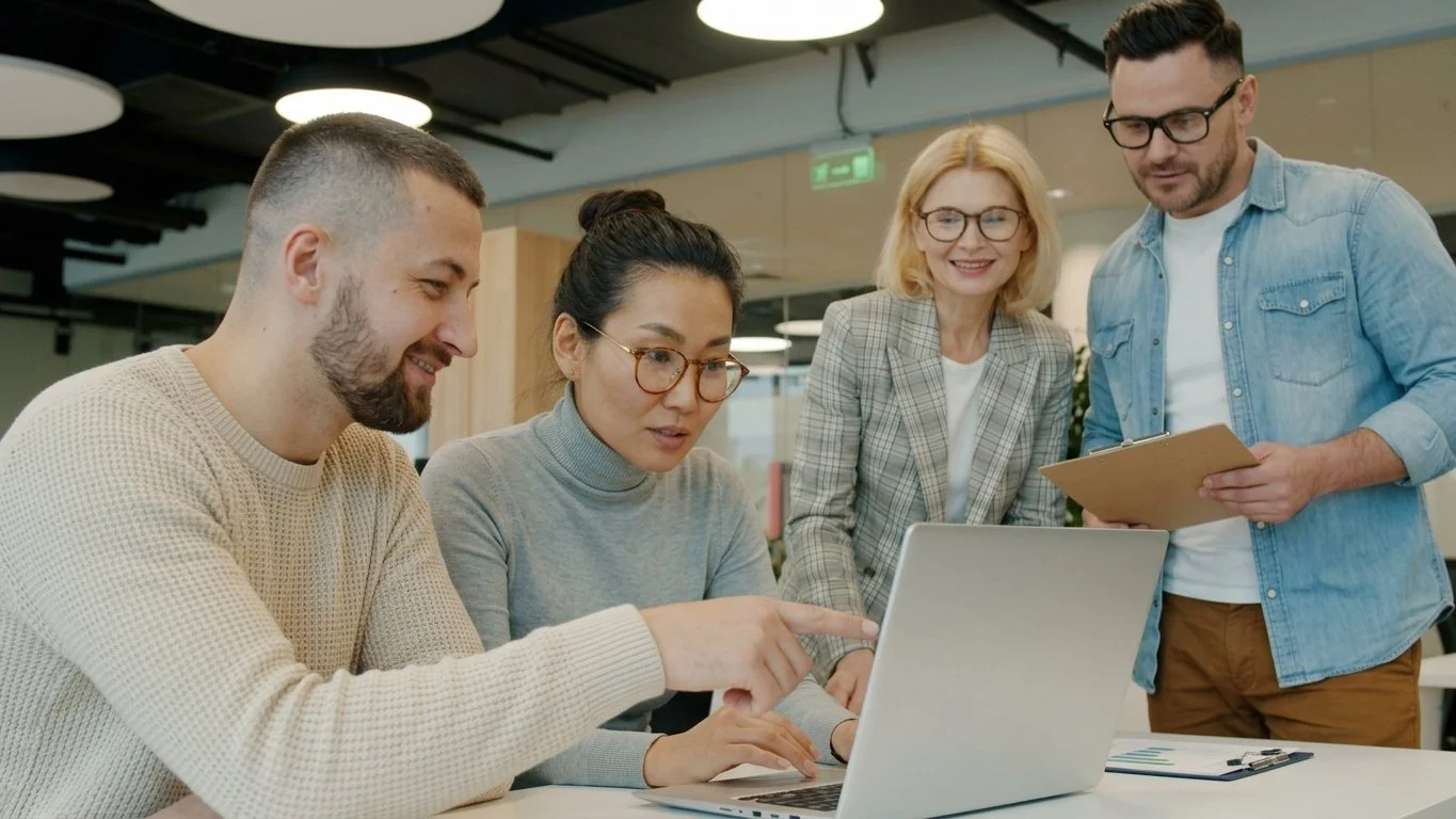 Diverse team of two women and two men collaborating around a laptop in a modern office.