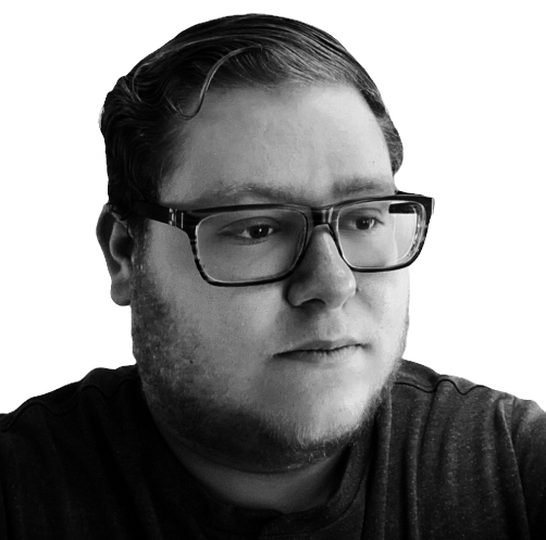Black and white photo of a young man with glasses, short hair, and a slight beard looking off to the side.