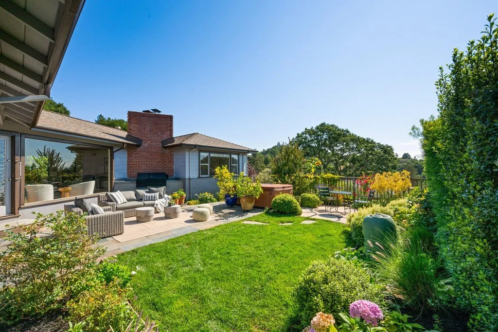 A backyard with a grassy lawn and outdoor patio furniture, potted plants, and garden decorations under a bright blue sky.