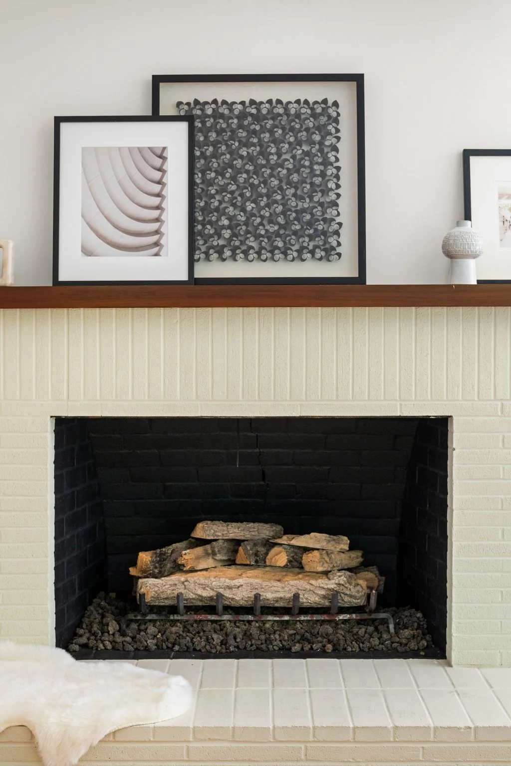 Living room fireplace with wood logs, framed black and white abstract art, and decorative items on mantel above.