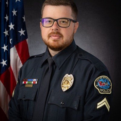 Portrait of a male police officer in uniform, standing in front of an American flag.