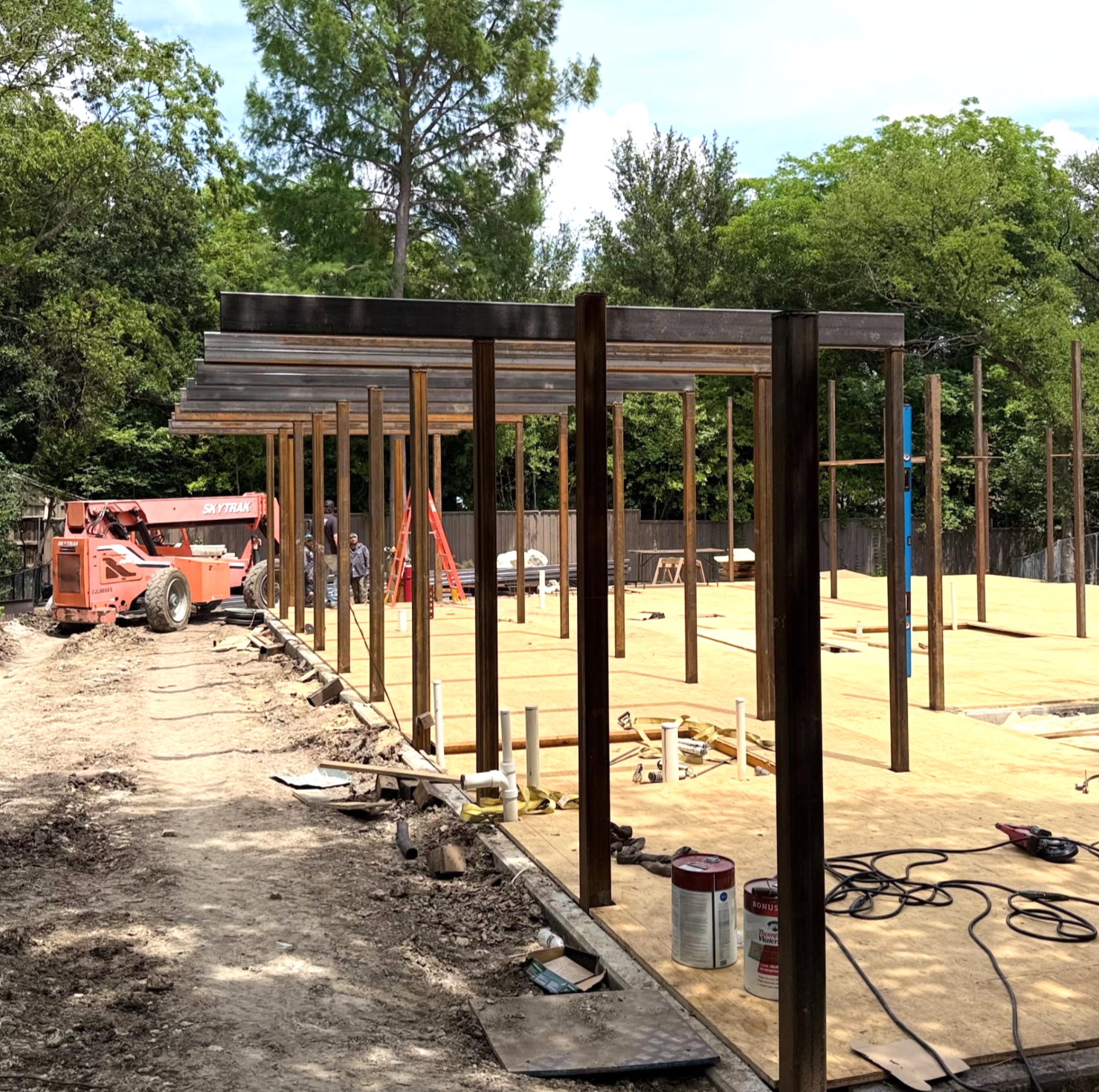 Custom structural steel framing being installed at a residential construction site with workers and equipment.