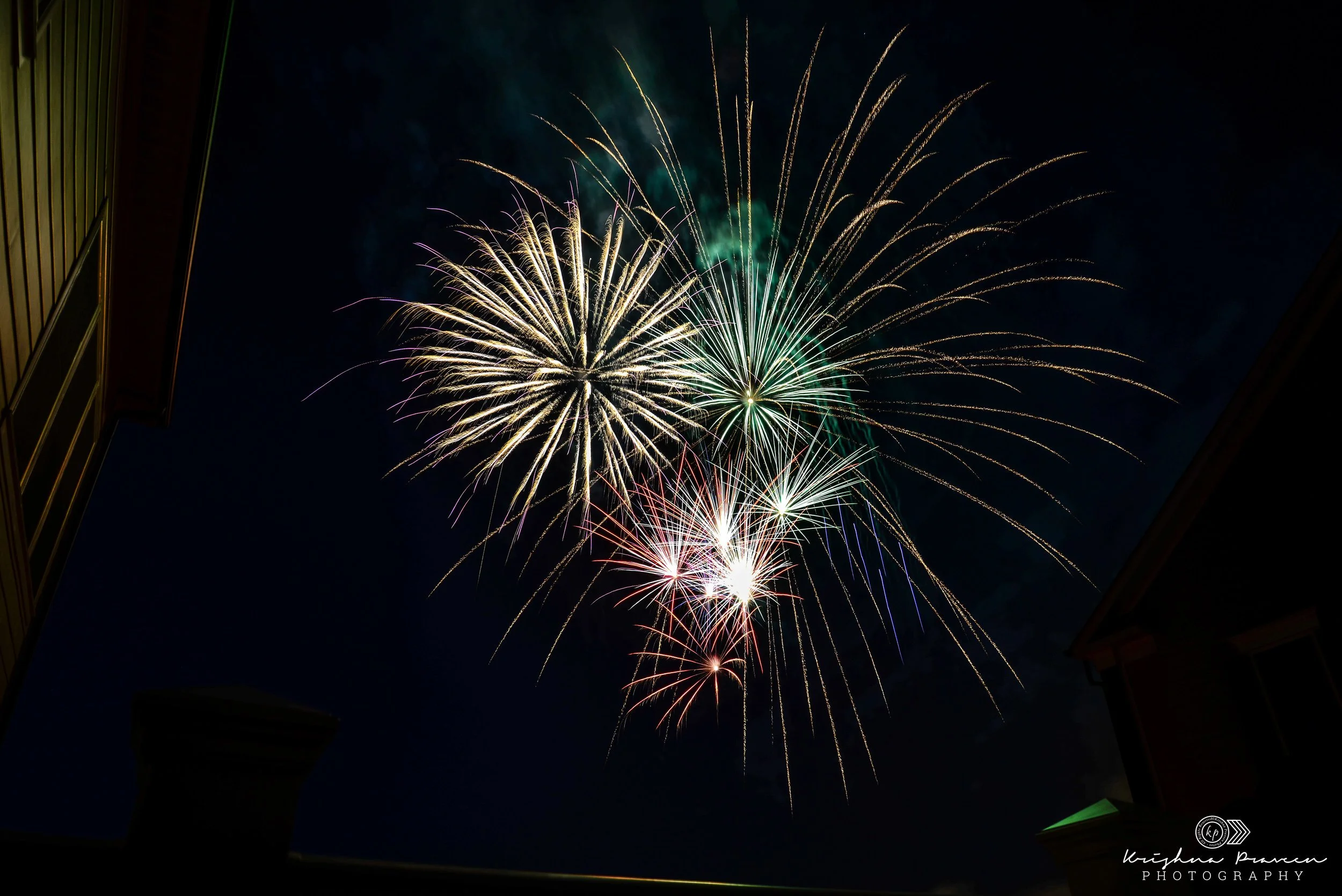 Colorful fireworks exploding in the night sky between two buildings.