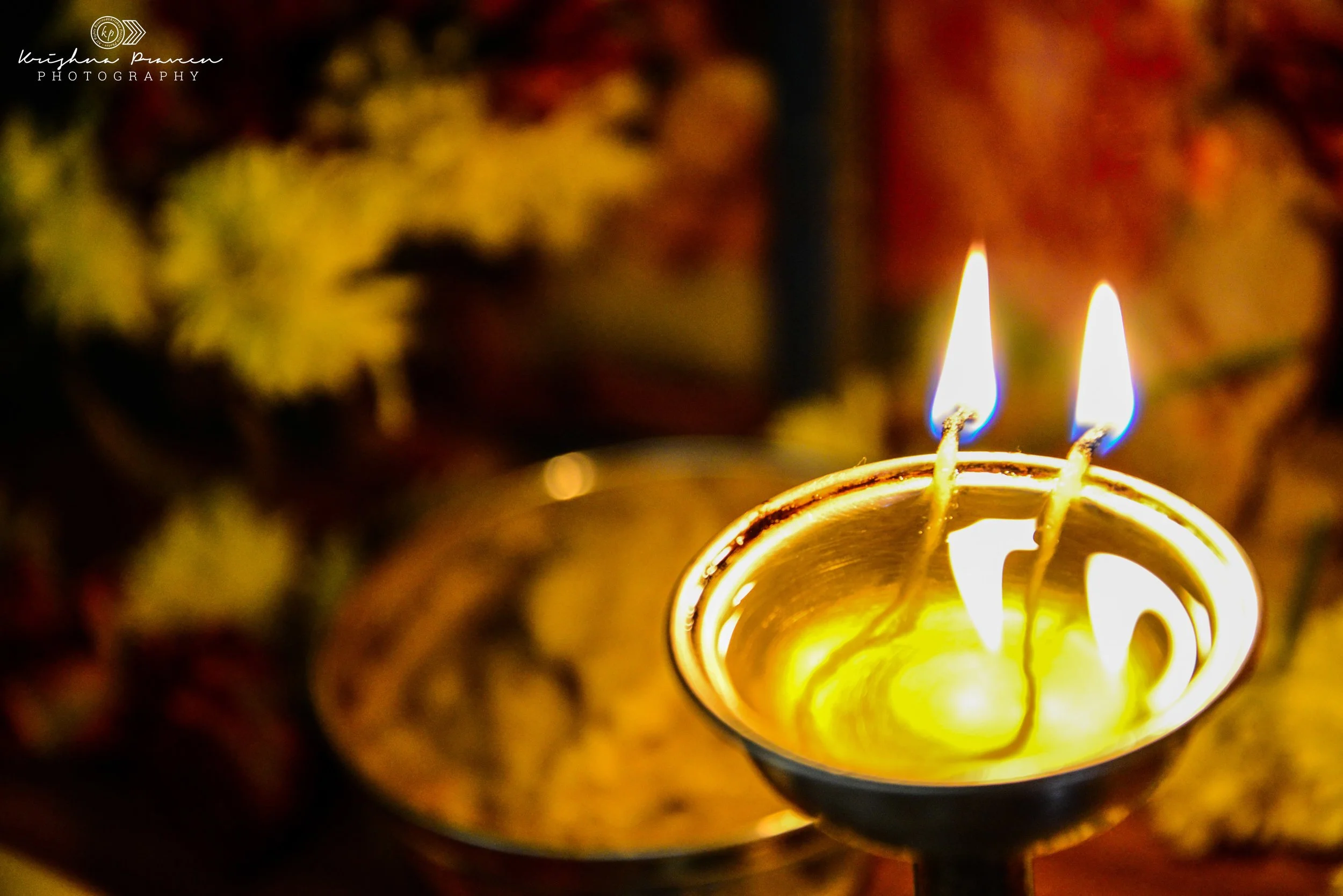 Close-up of a lit candle with flames burning, blurred colorful background with autumn leaves.