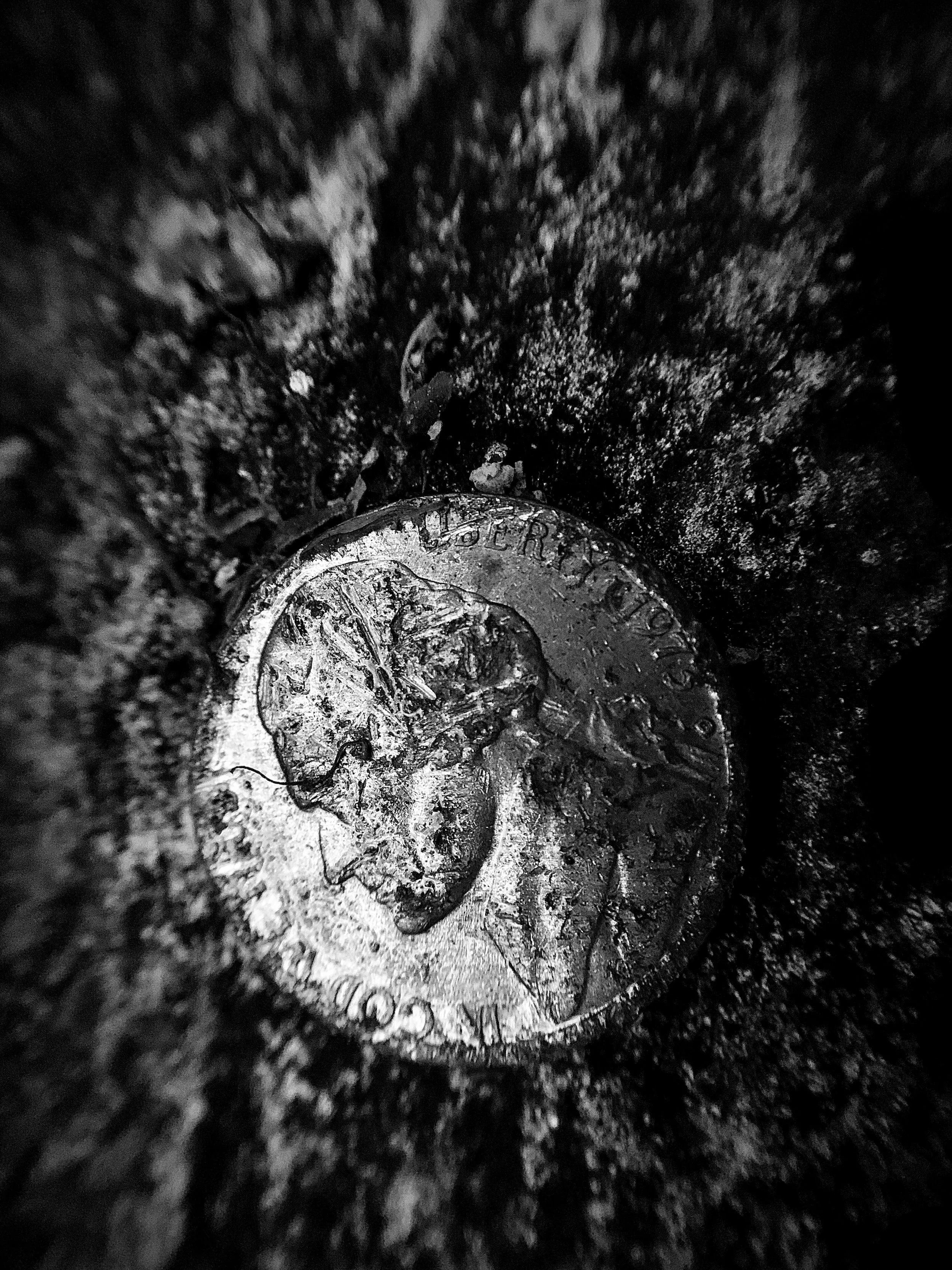 Close-up shot of a U.S. quarter coin partially buried in dirt or soil, with the word 'LIBERTY' visible on the coin.