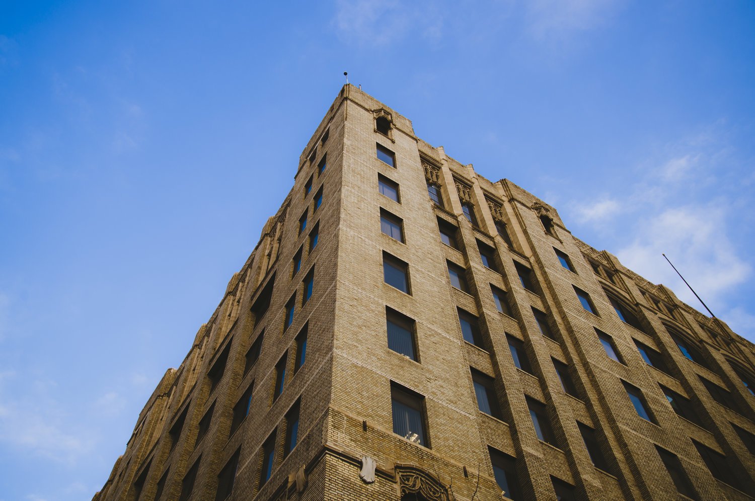 A tall, beige brick building with multiple windows against a blue sky with light clouds.