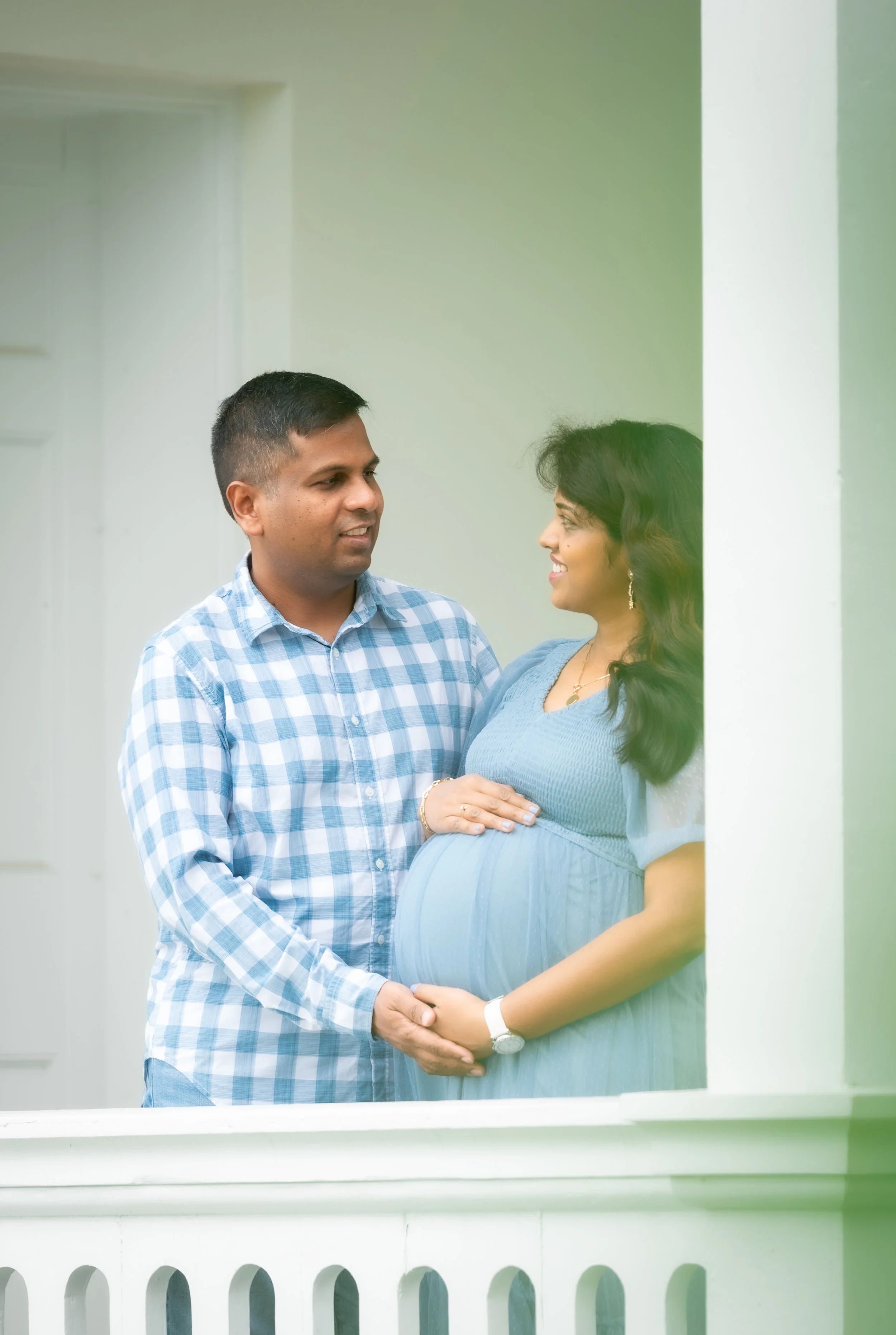 Expecting couple, the man and pregnant woman, standing on balcony, holding hands, smiling, indoors.