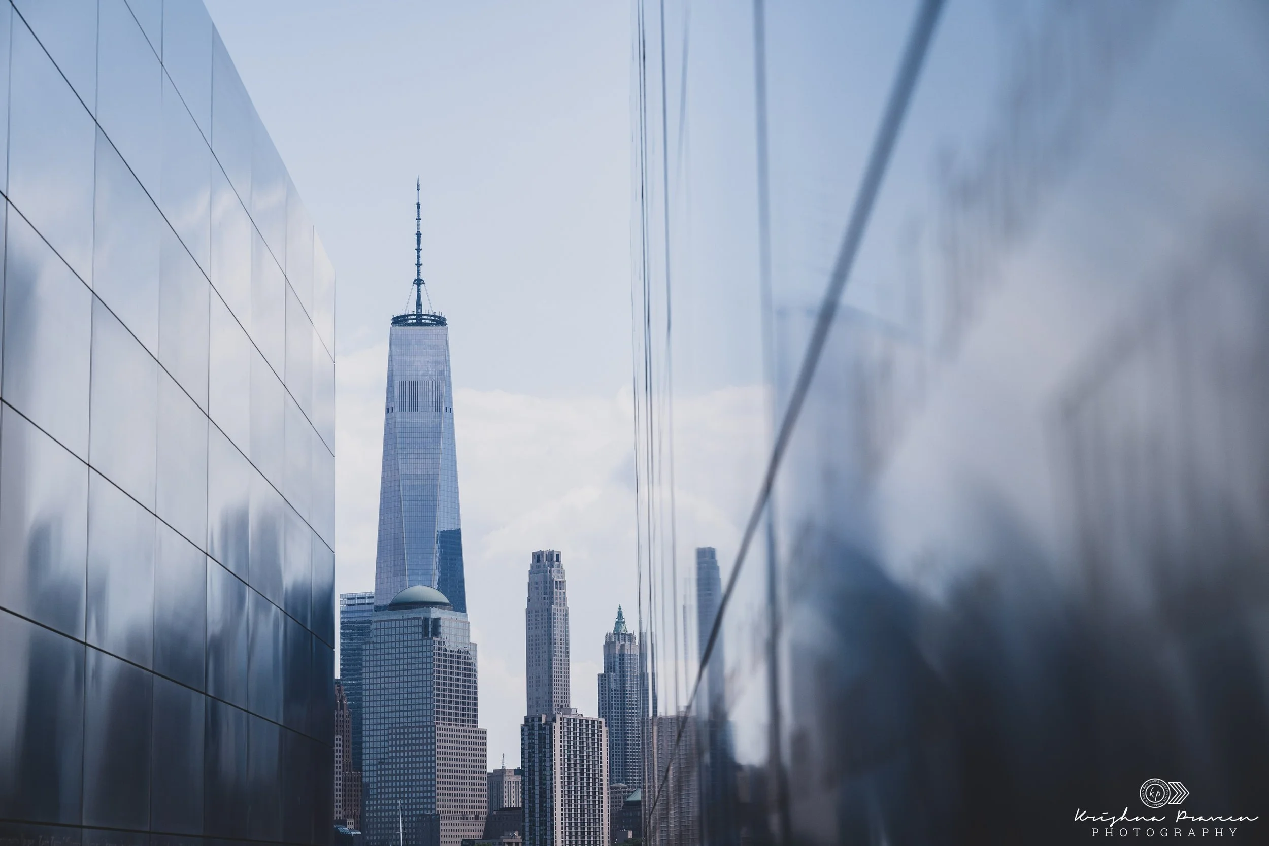 Skyscrapers in a city seen through reflective building surfaces with cloudy sky overhead.