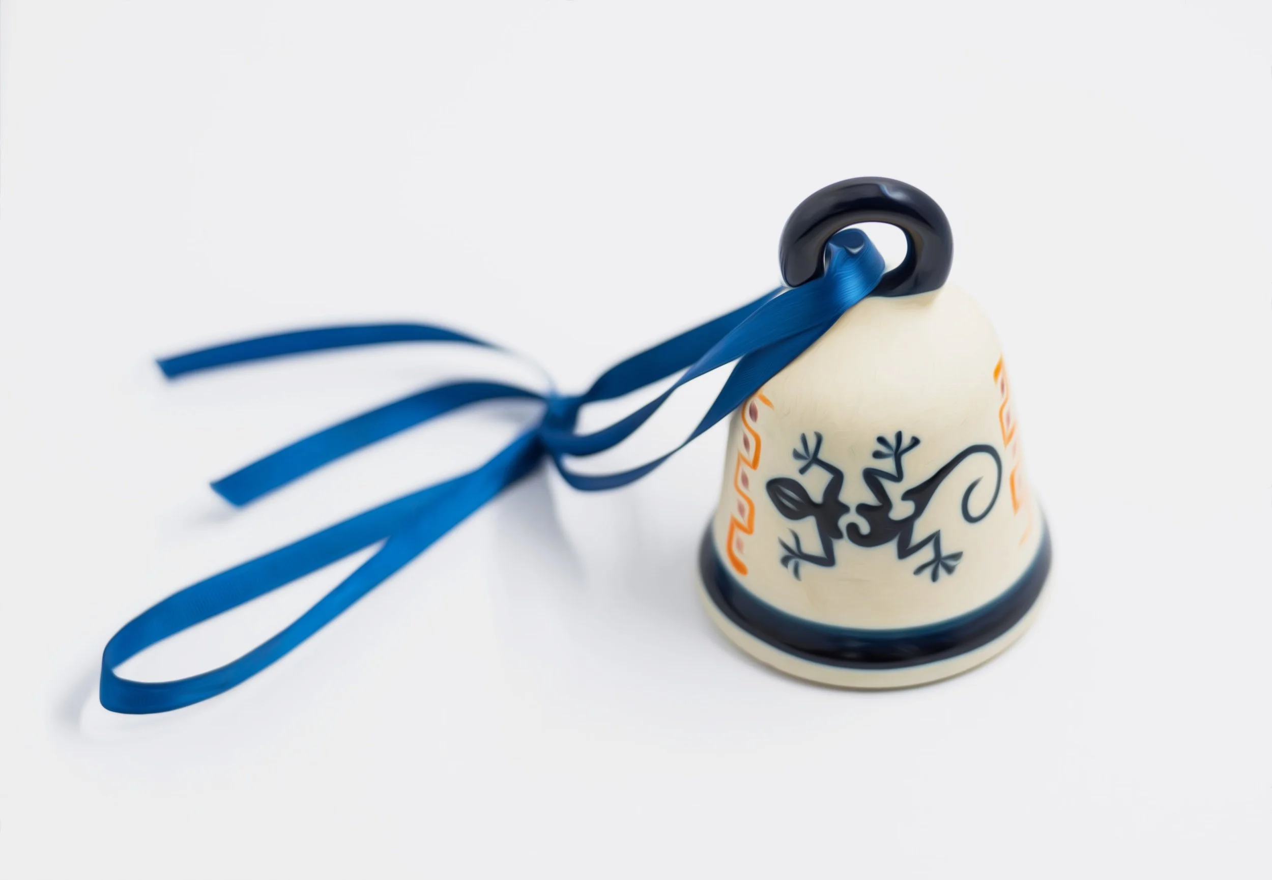 A ceramic bell-shaped object with black decorative designs and orange accents, tied with a blue ribbon.