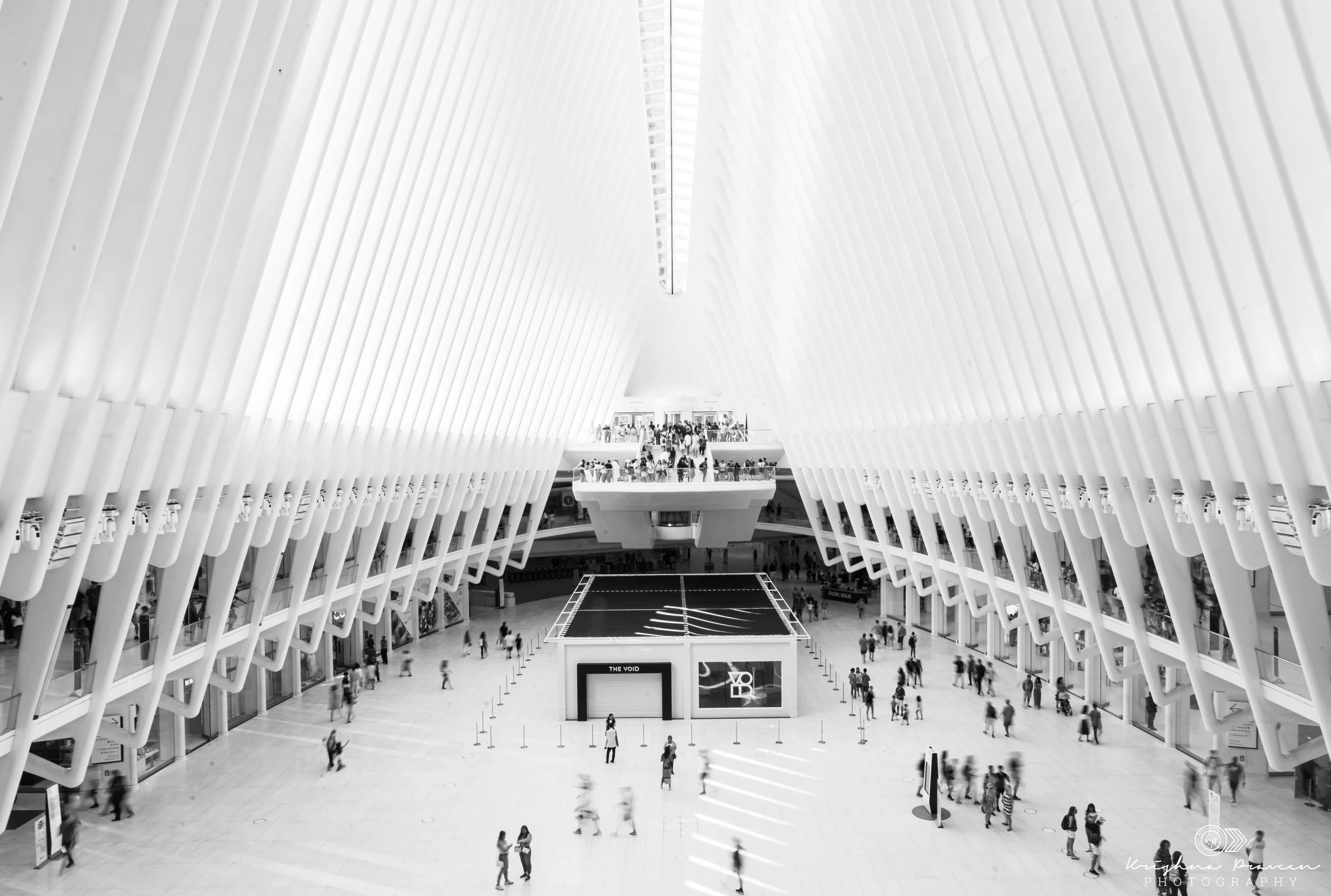 Interior of a modern architectural building with high arched white walls, a central court, and people walking and gathering.