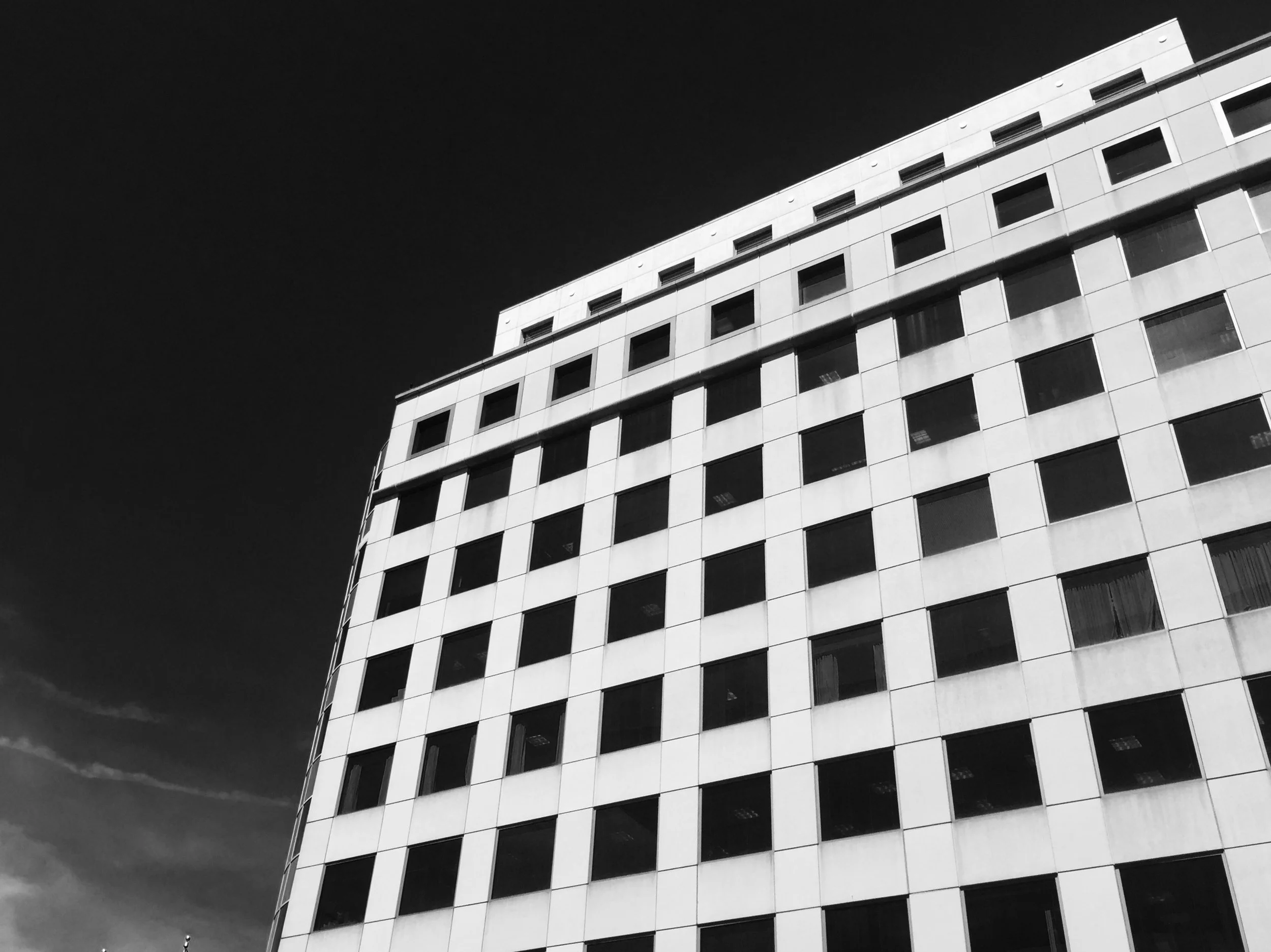 A modern multi-story building with a curved facade featuring numerous rectangular windows, set against a dark sky.
